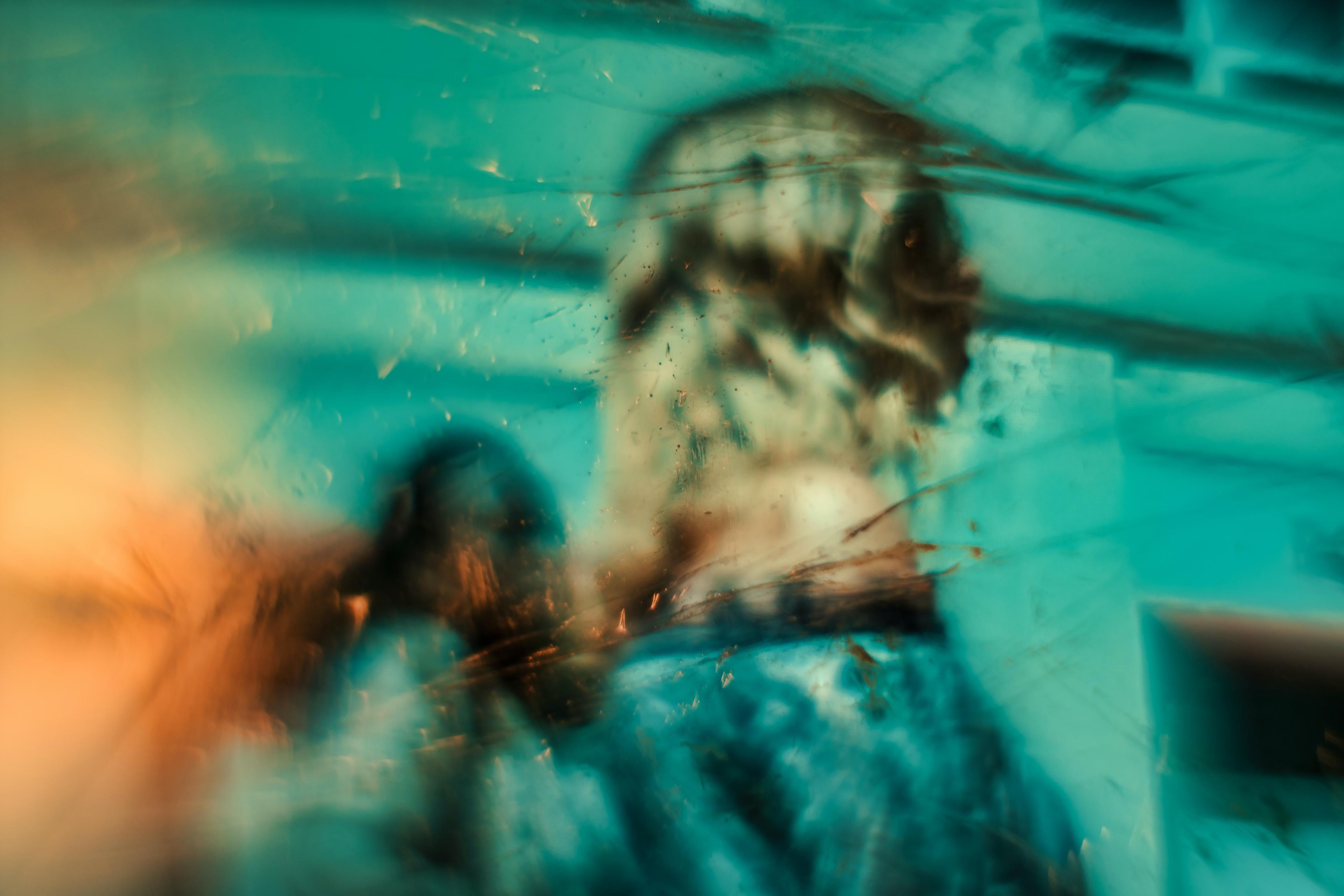 Abstract painting with blurred figures in teal and orange tones suggesting motion and mystery.