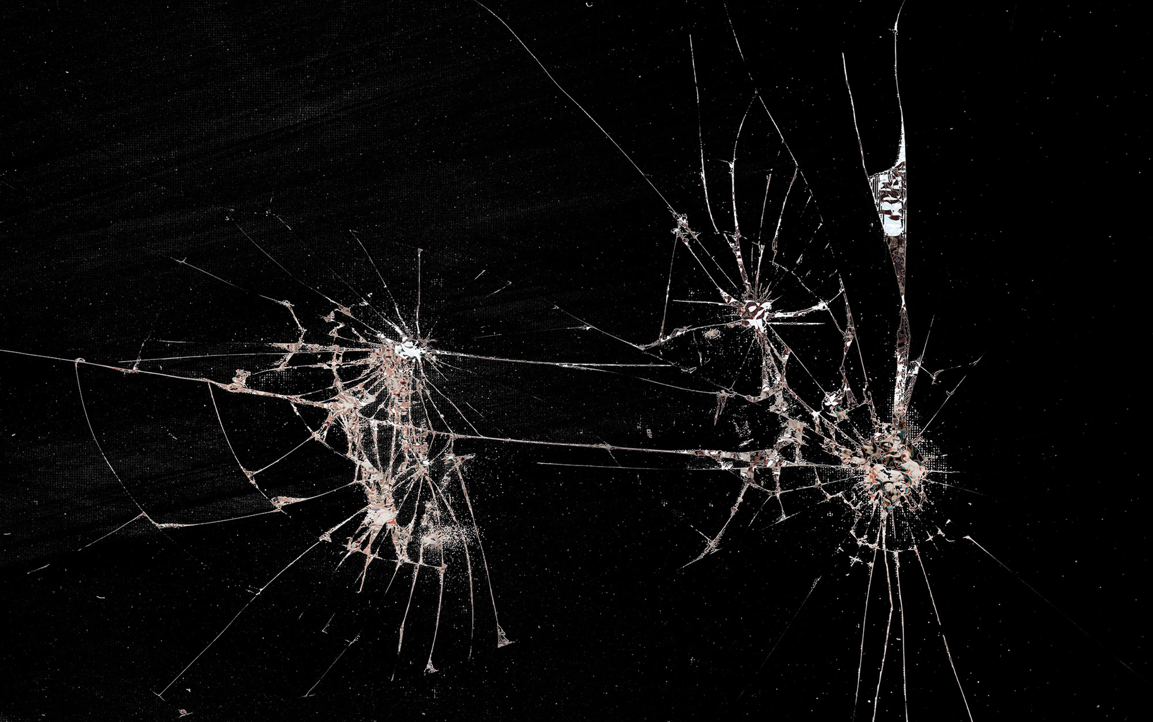 Photo of shattered glass with multiple cracks against a black background.