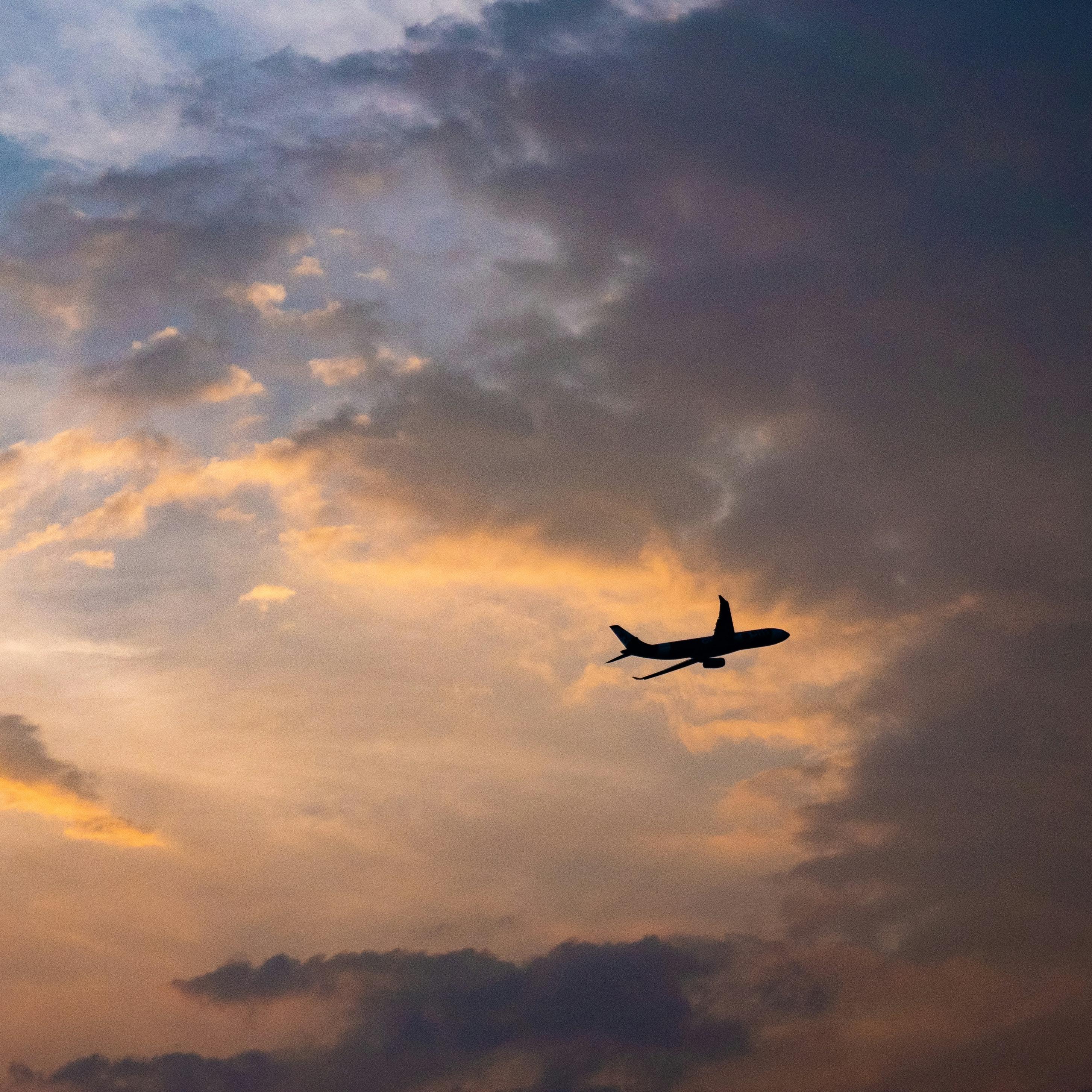 An aeroplane seen in silhouette, flying against a dramatic sunset sky with clouds.