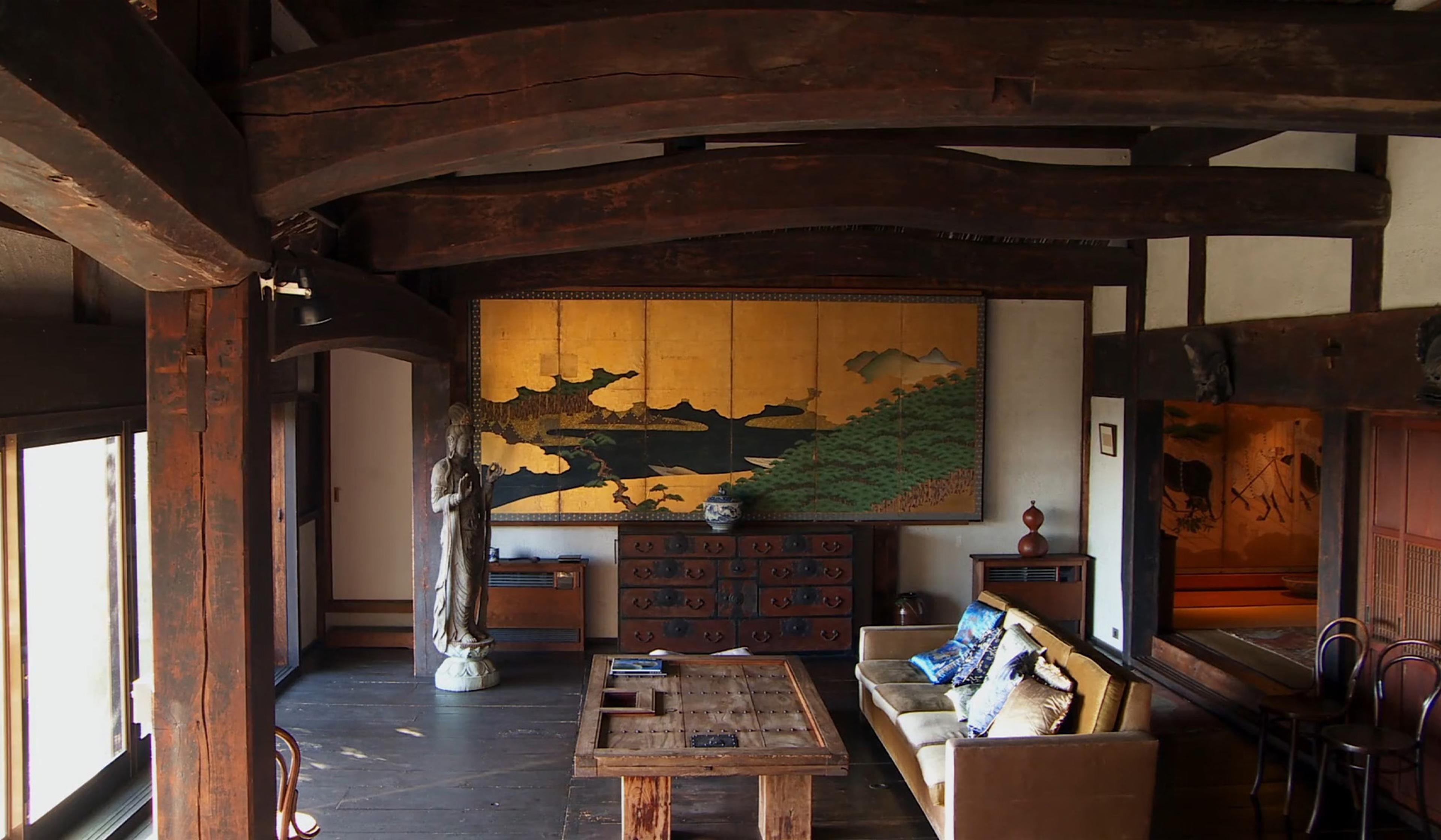 Interior of a traditional Japanese room with wooden beams, a painting, a statue, a sofa, and wooden furniture.