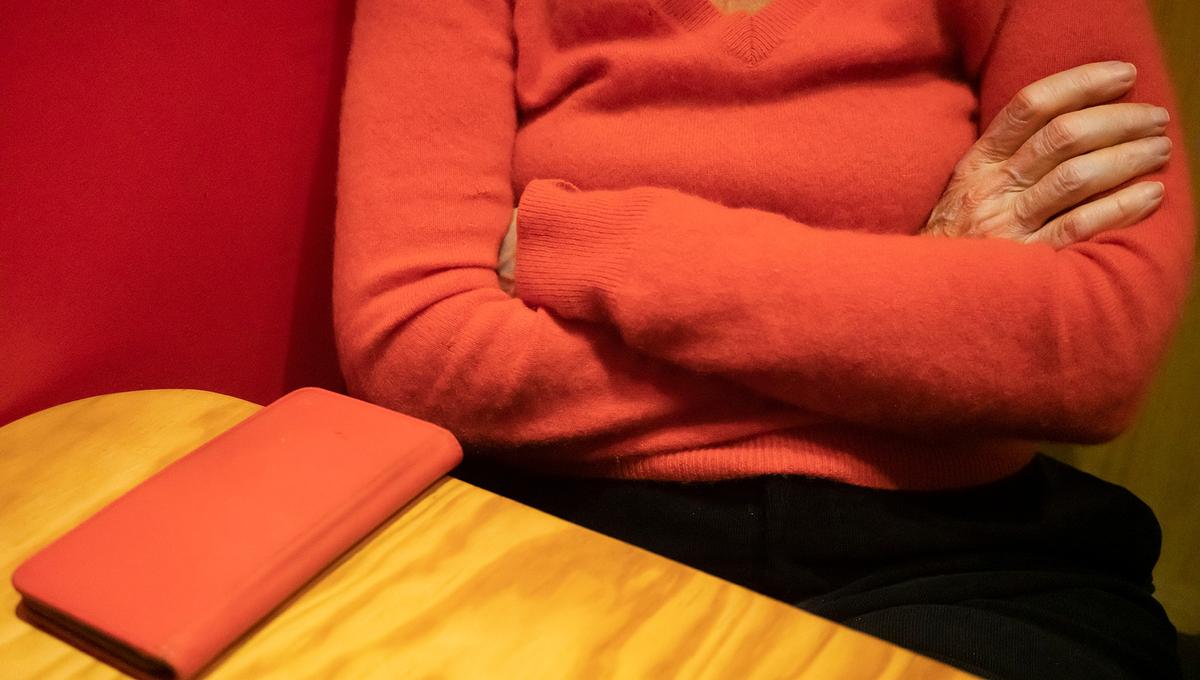 A person in an orange sweater with arms crossed, sitting at a table with a closed orange phone case on it.