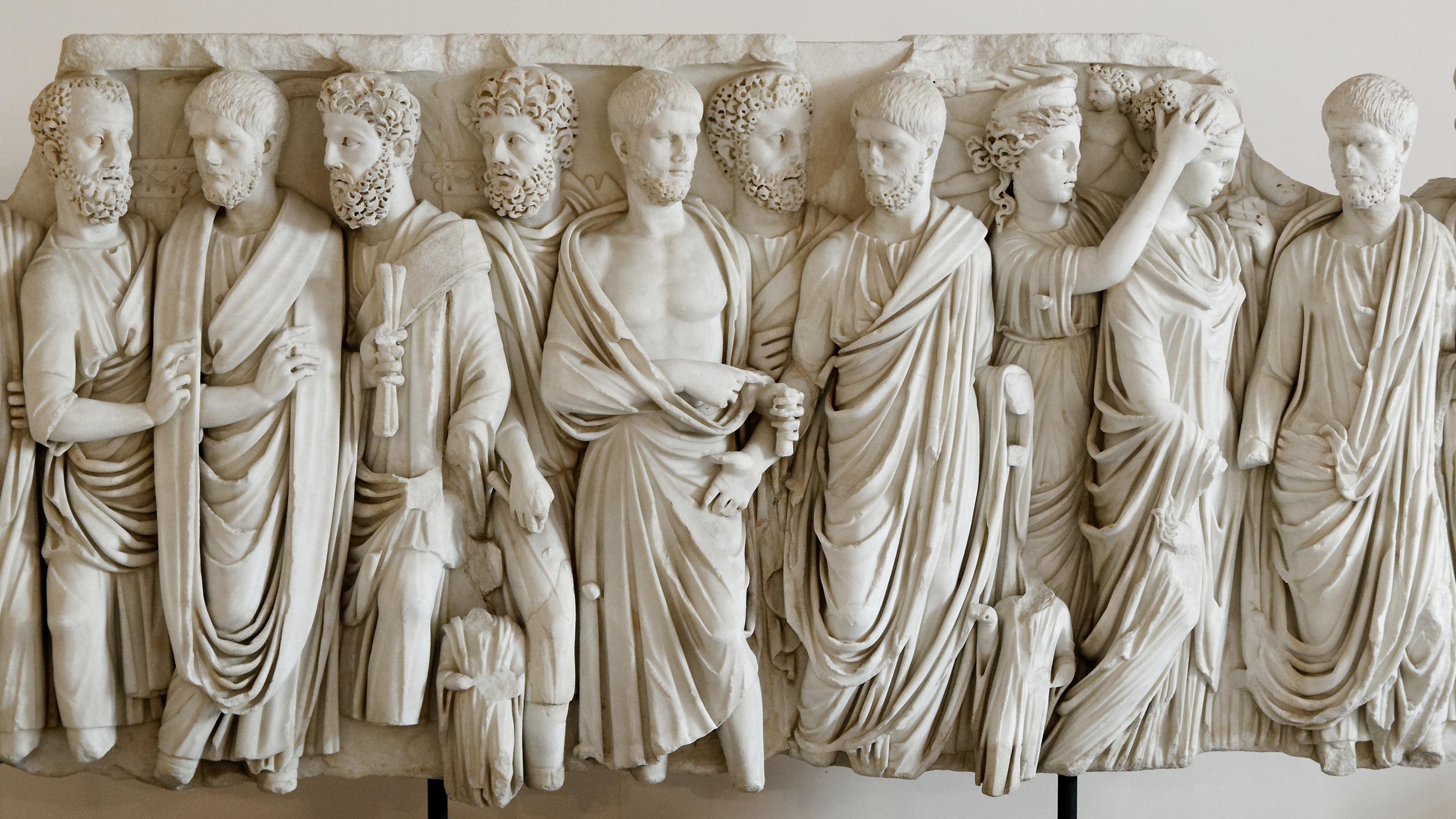 Marble relief sculpture of eleven ancient figures in draped clothing, showcasing detailed expressions and intricate designs.