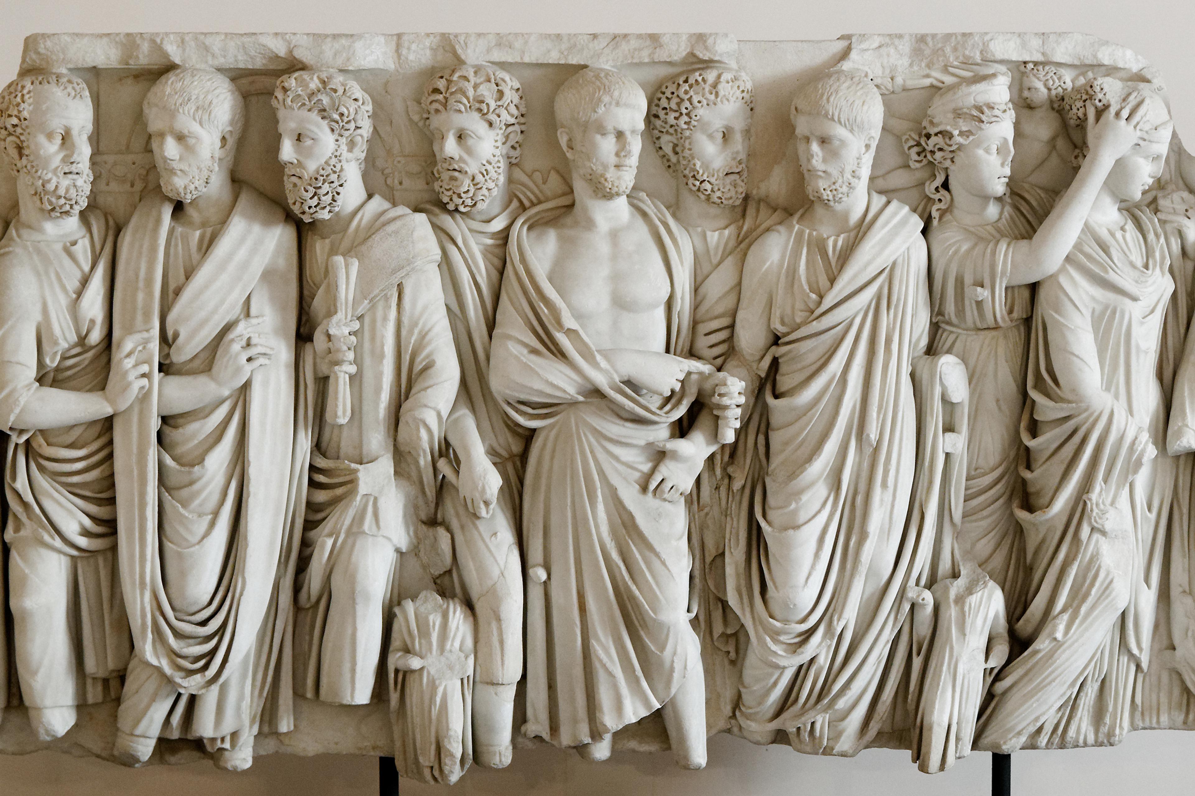 Marble relief sculpture of eleven ancient figures in draped clothing, showcasing detailed expressions and intricate designs.