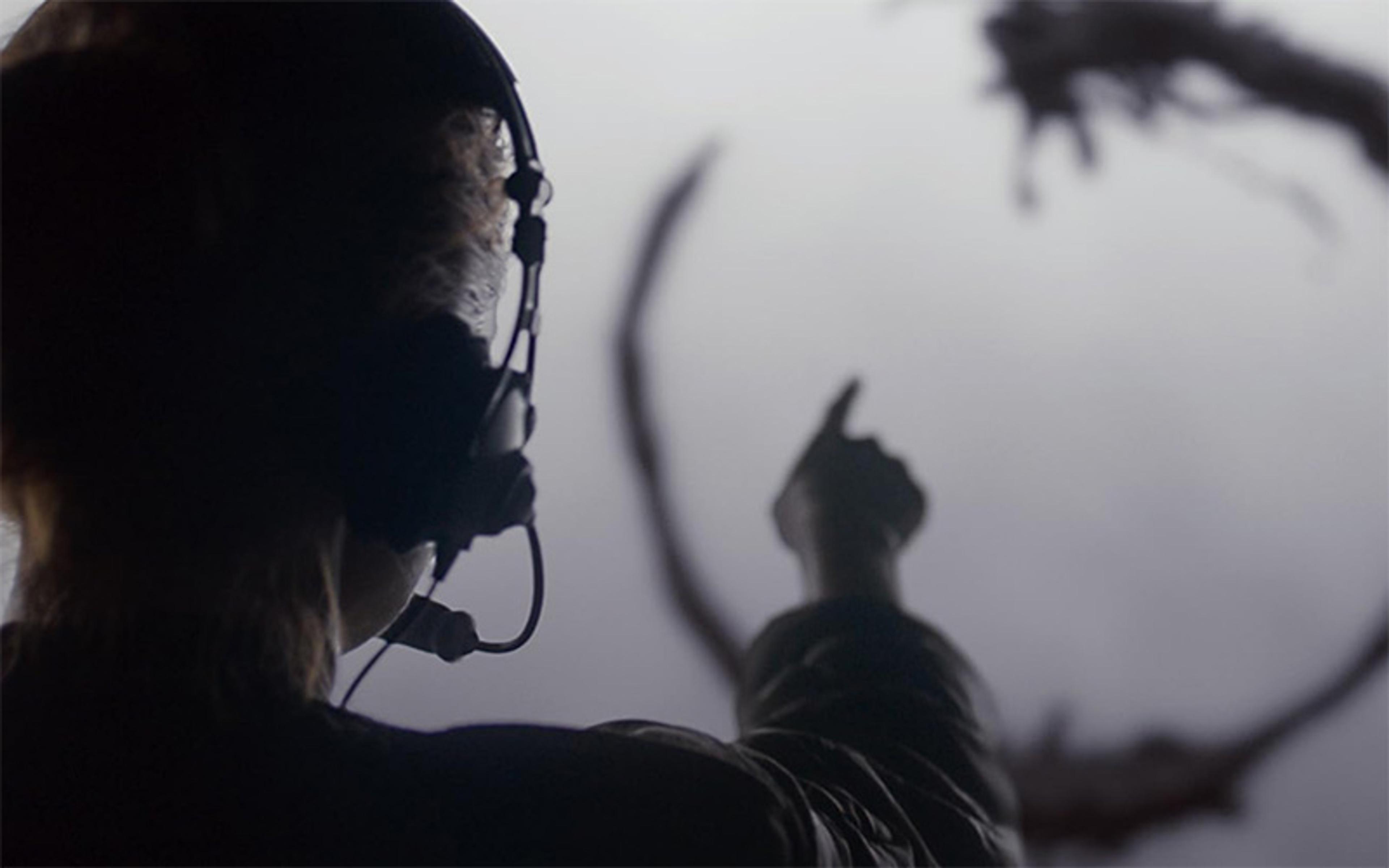 A person wearing headphones pointing at a circular pattern out of focus in the distance, viewed from behind.