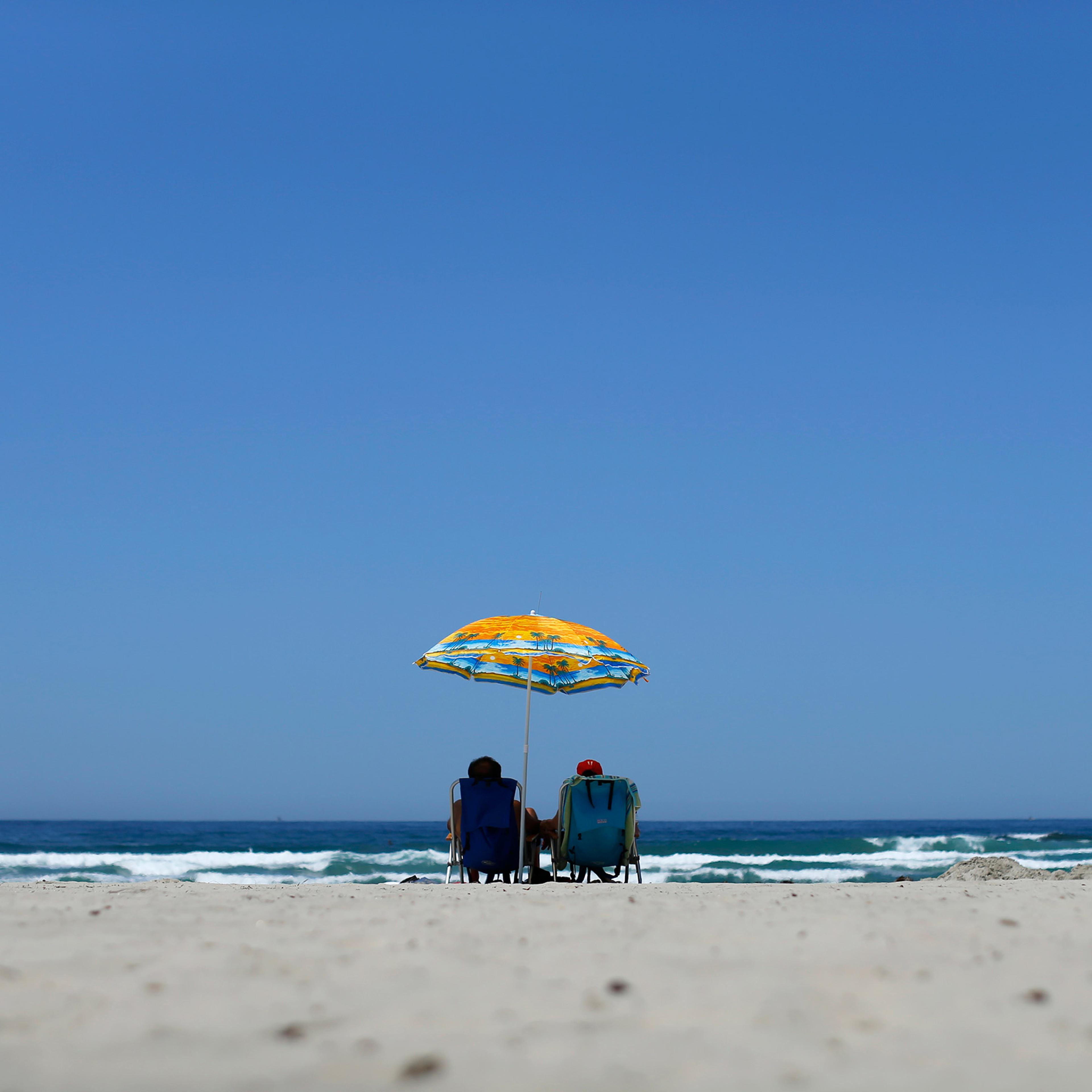A couple sit in deckchairs beneath a parasol gazing out at the ocean