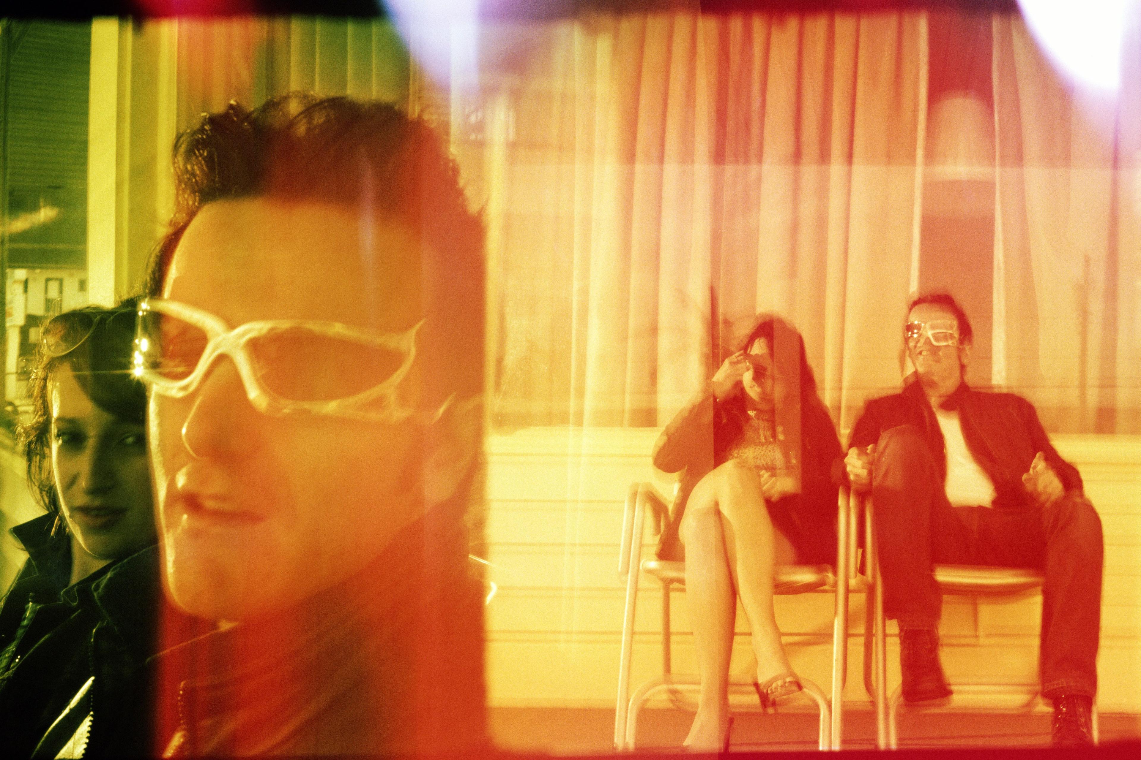 Colourful photo with three people in sunglasses. Blurred effect, room number 101 visible, two seated in the background.
