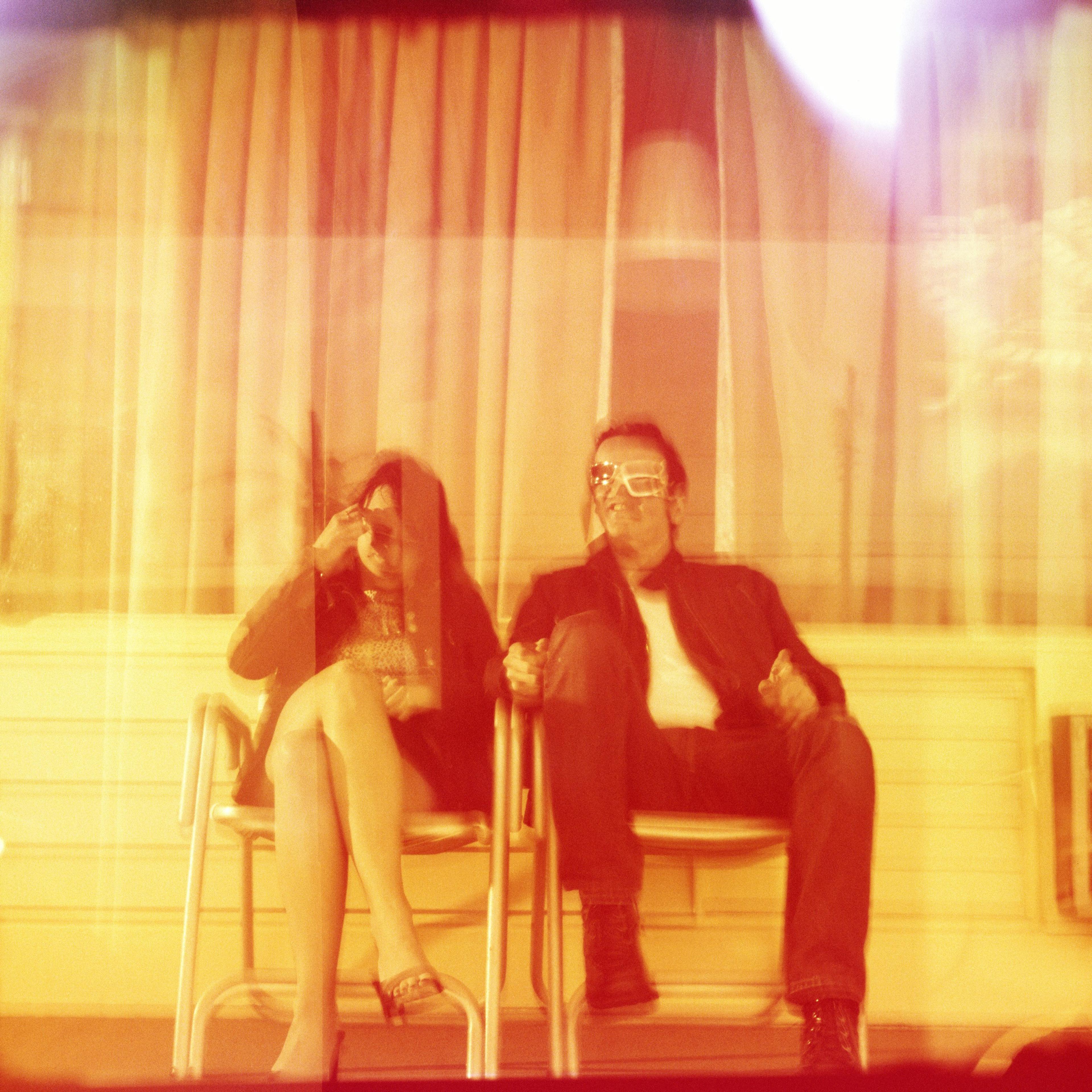 Colourful photo with three people in sunglasses. Blurred effect, room number 101 visible, two seated in the background.