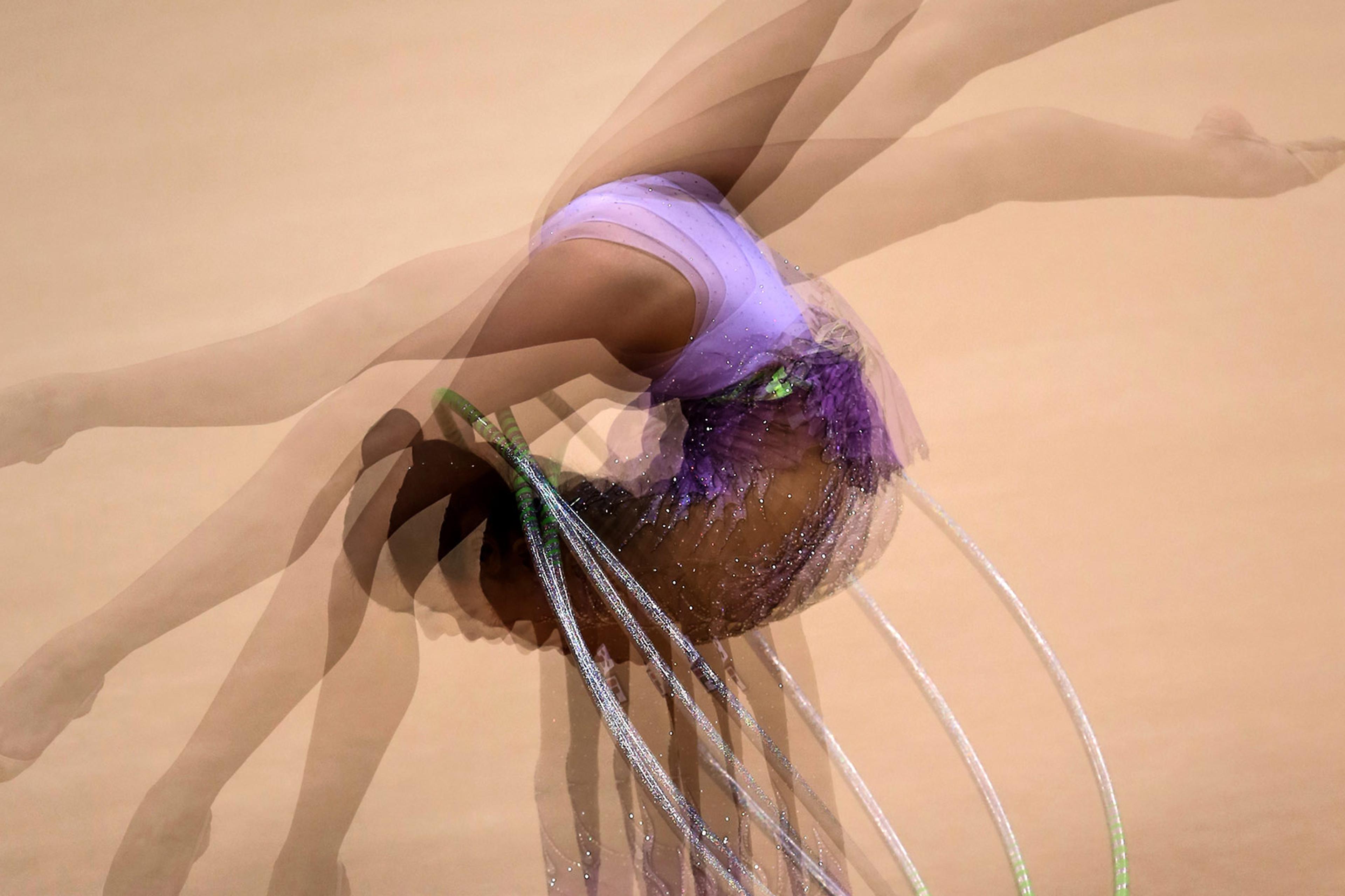 A gymnast in a purple leotard mid-performance, captured with a motion blur effect, showing multiple overlapping images of her movement.