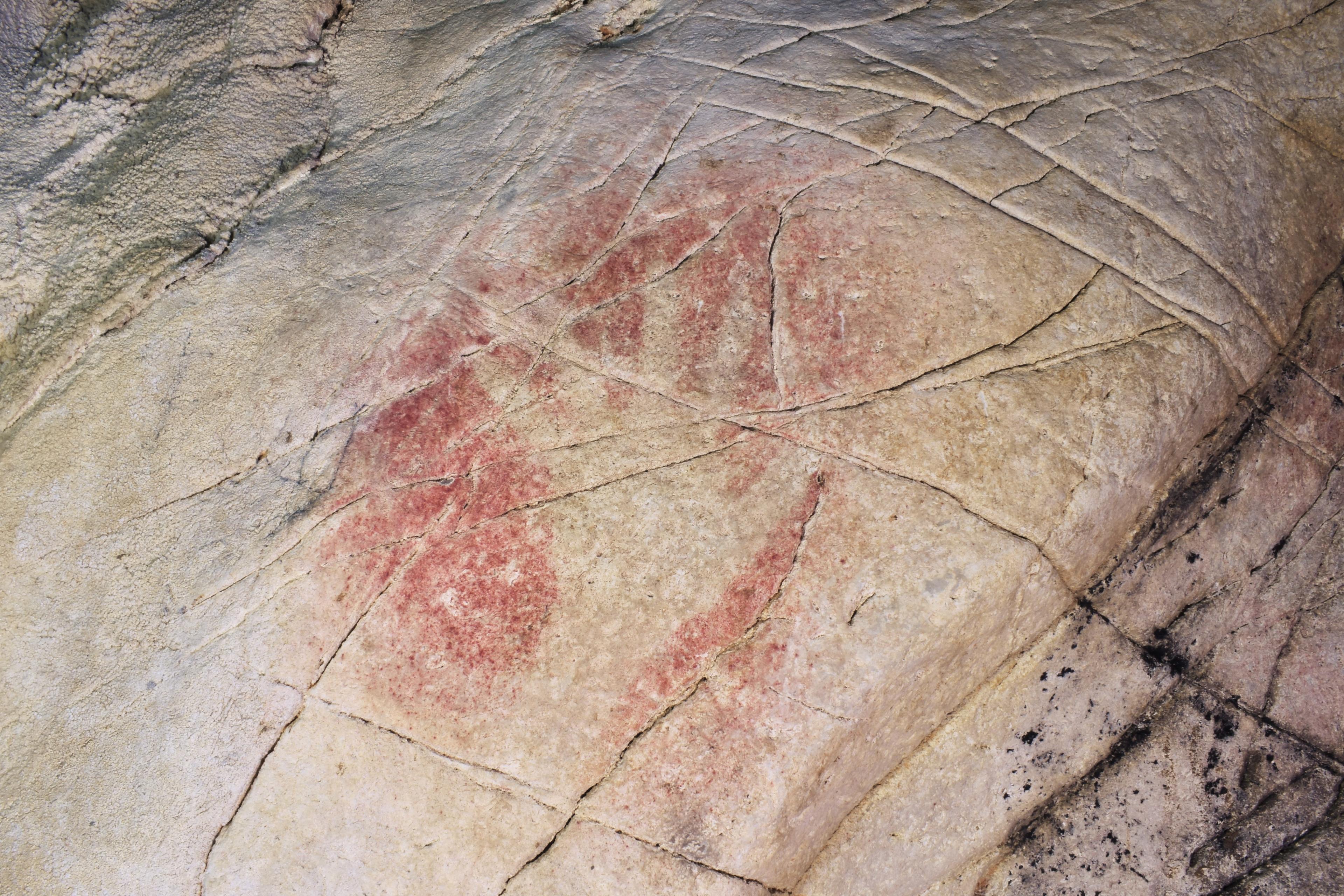 Rock art painting with red pigments on a weathered stone surface showing abstract shapes and natural cracks.