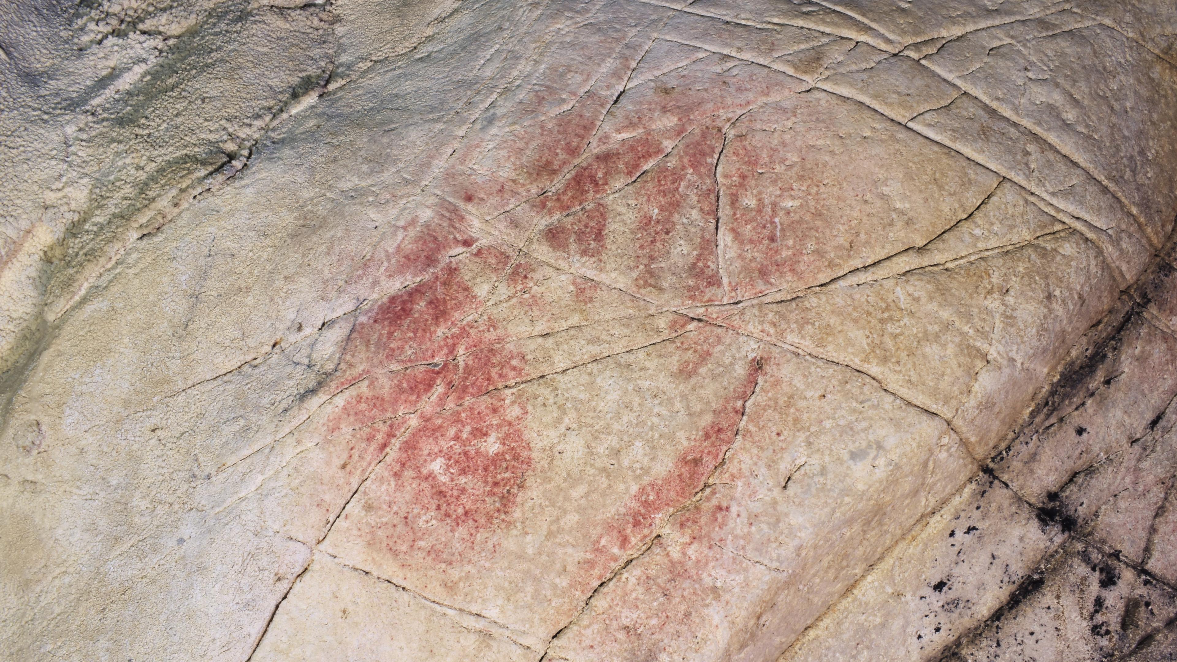 Rock art painting with red pigments on a weathered stone surface showing abstract shapes and natural cracks.