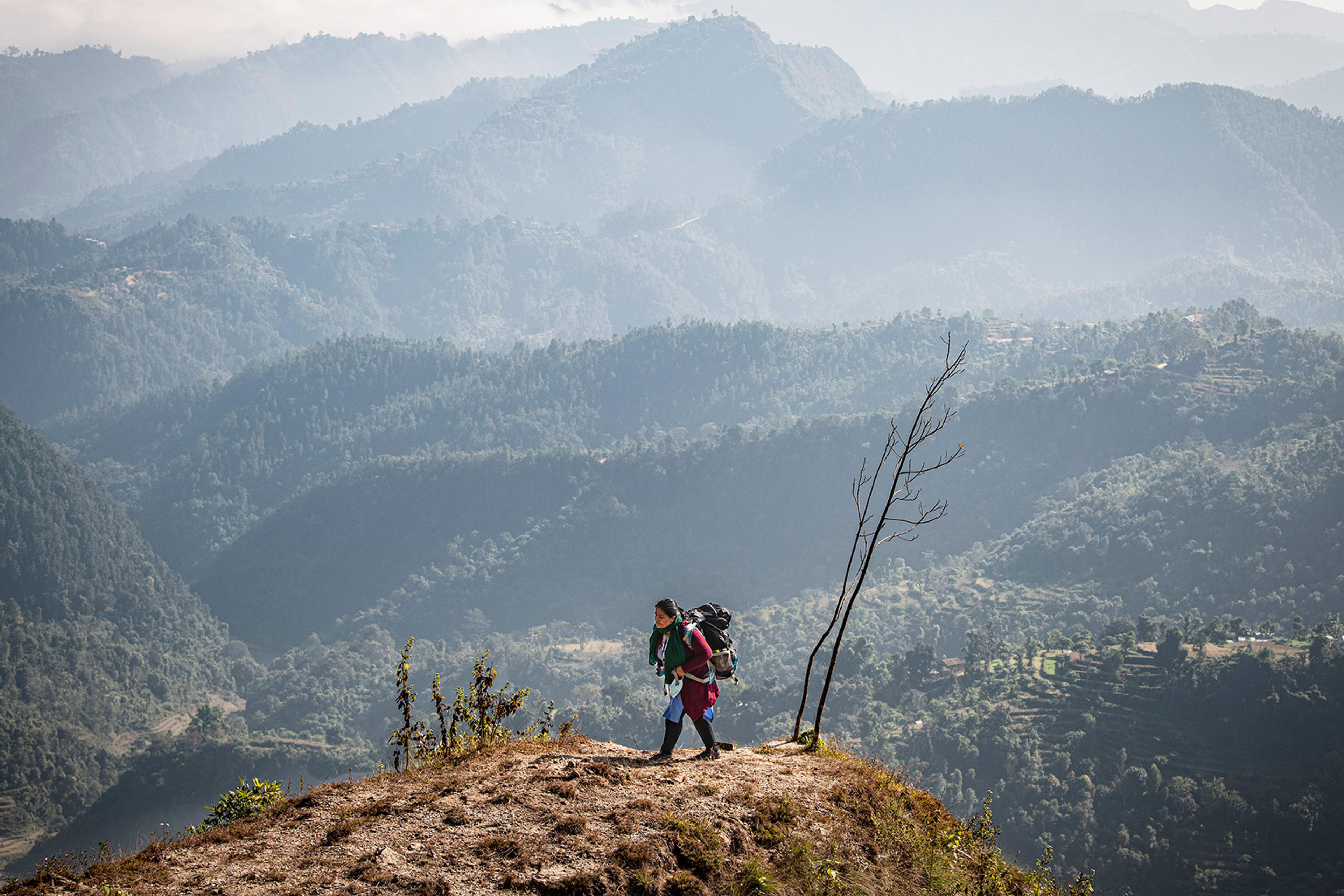 Hiker with a large backpack walking along a ridge with misty mountains in the background.