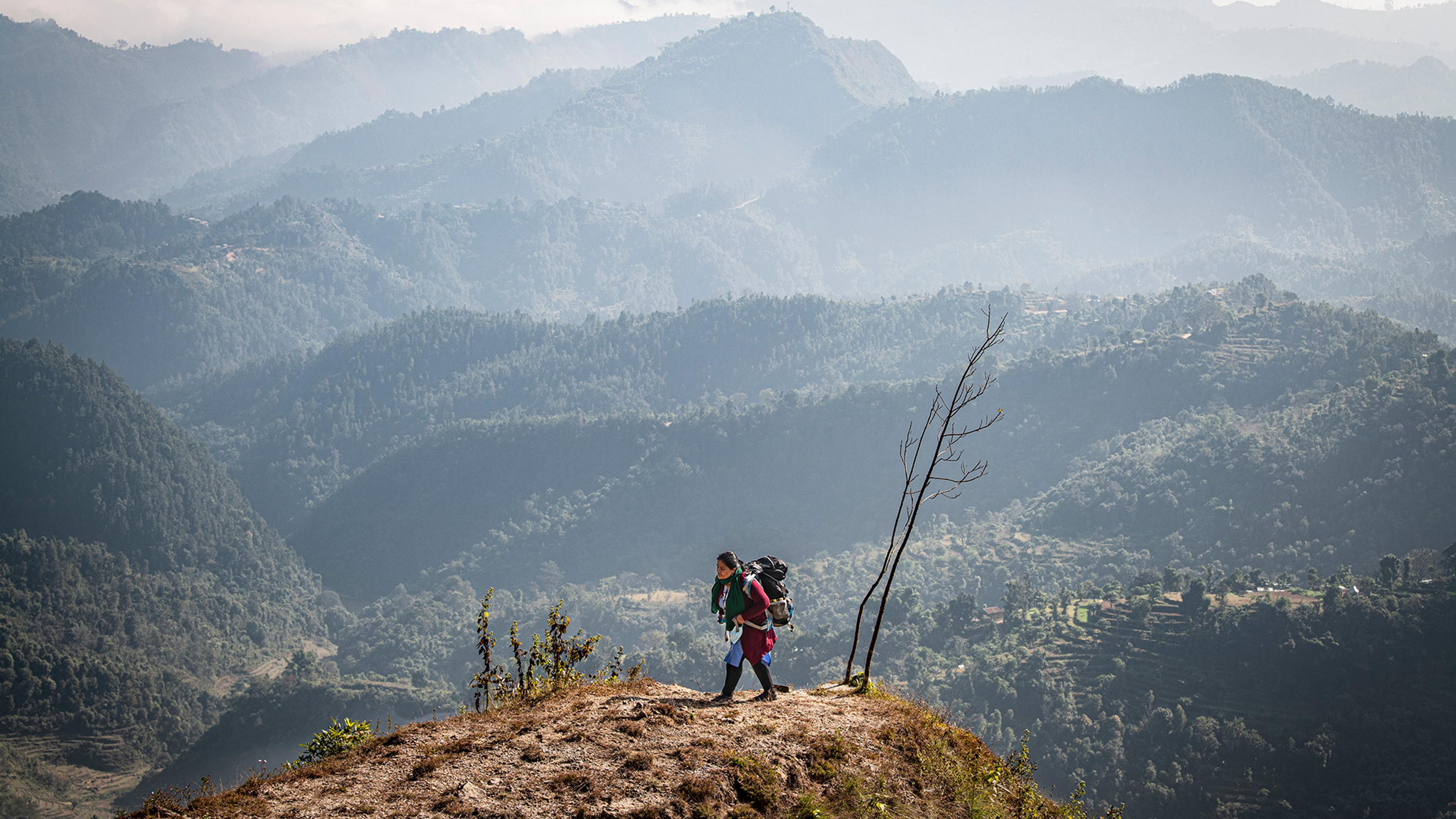 Hiker with a large backpack walking along a ridge with misty mountains in the background.