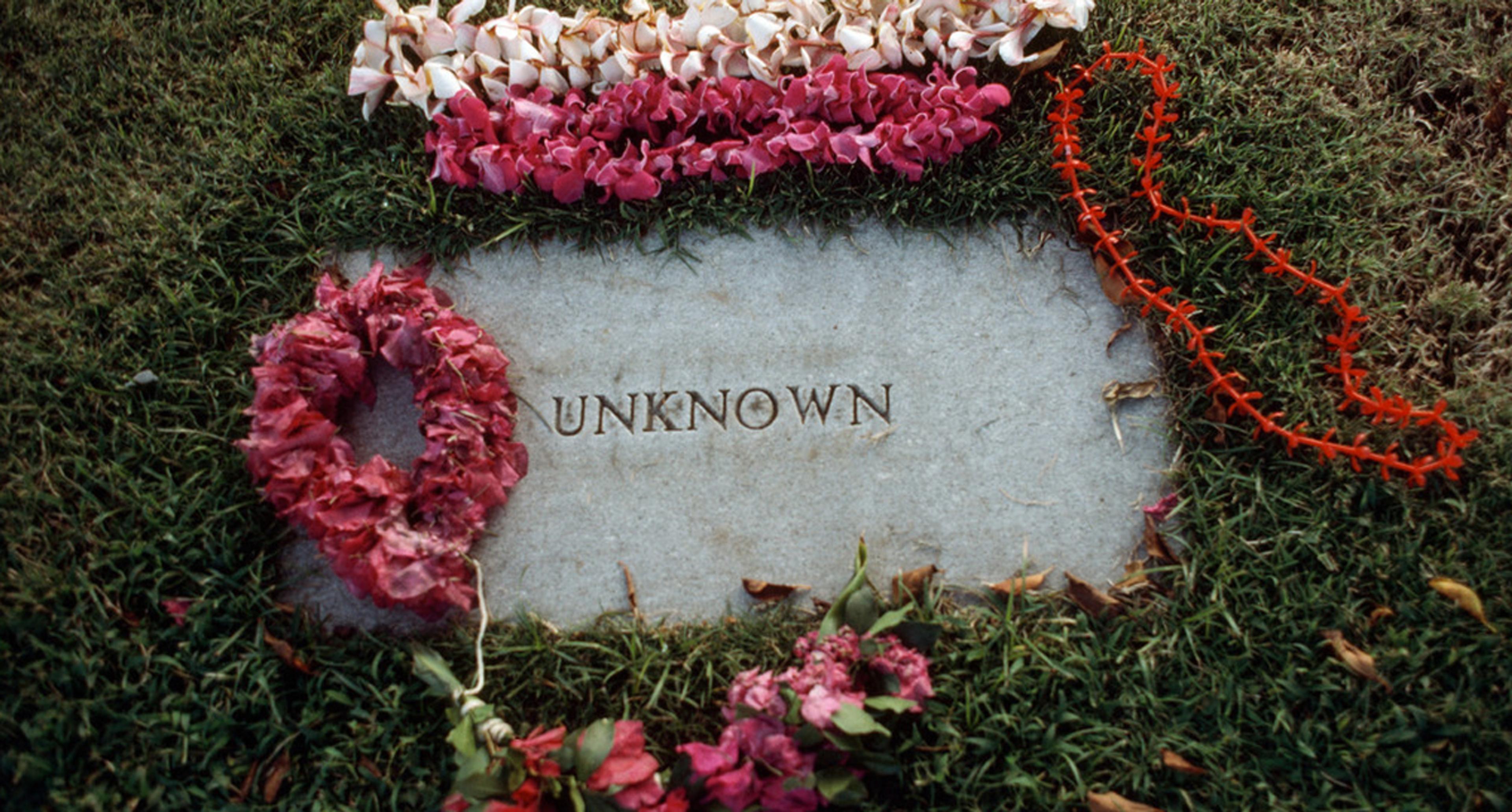 A gravestone labelled ‘Unknown’ surrounded by red, pink and white flowers on green grass.