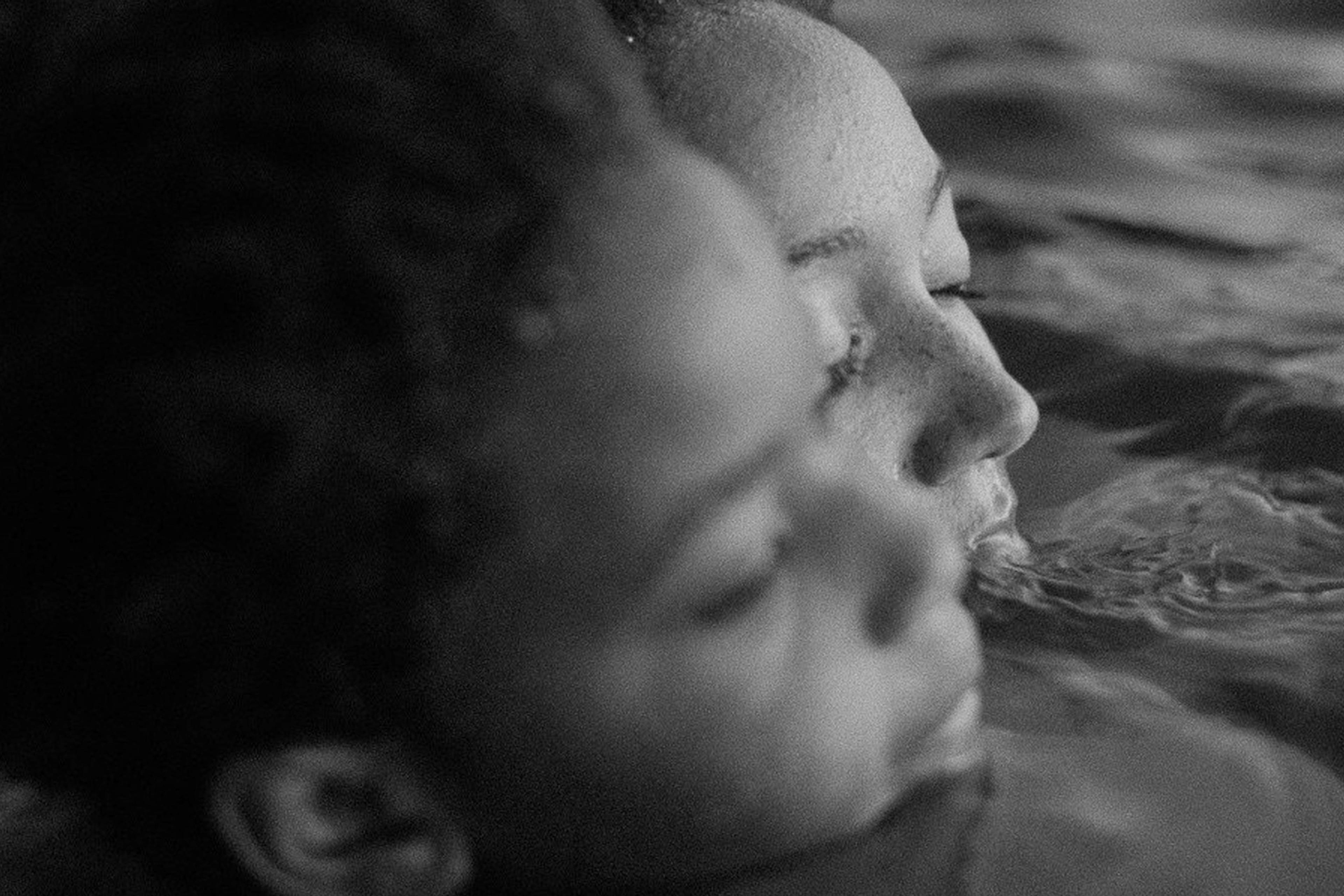 Black and white photo of two people close together in water, eyes closed and relaxed.