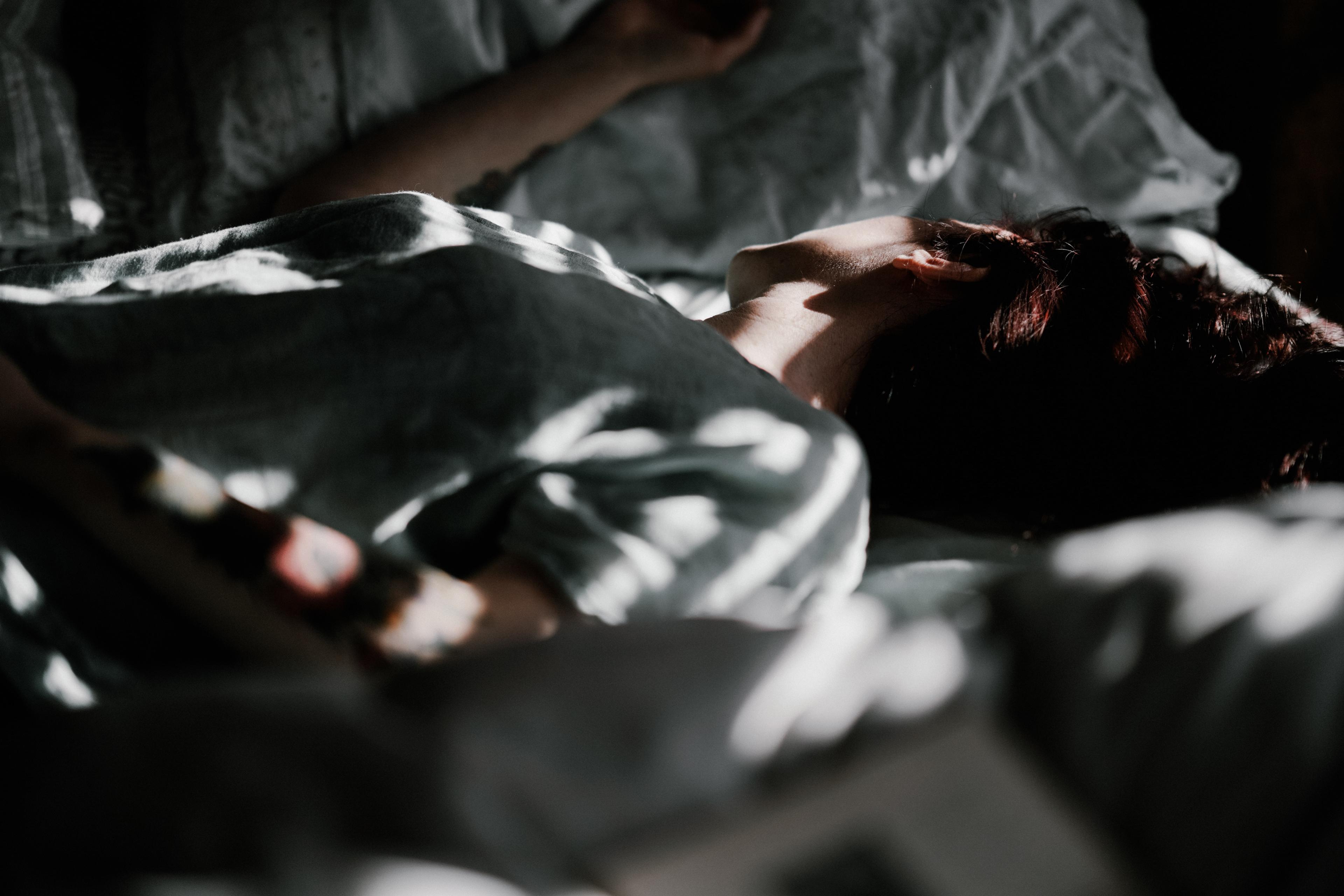 Photo of a person lying in bed under soft light and shadows, with focus on their neck and shoulder.
