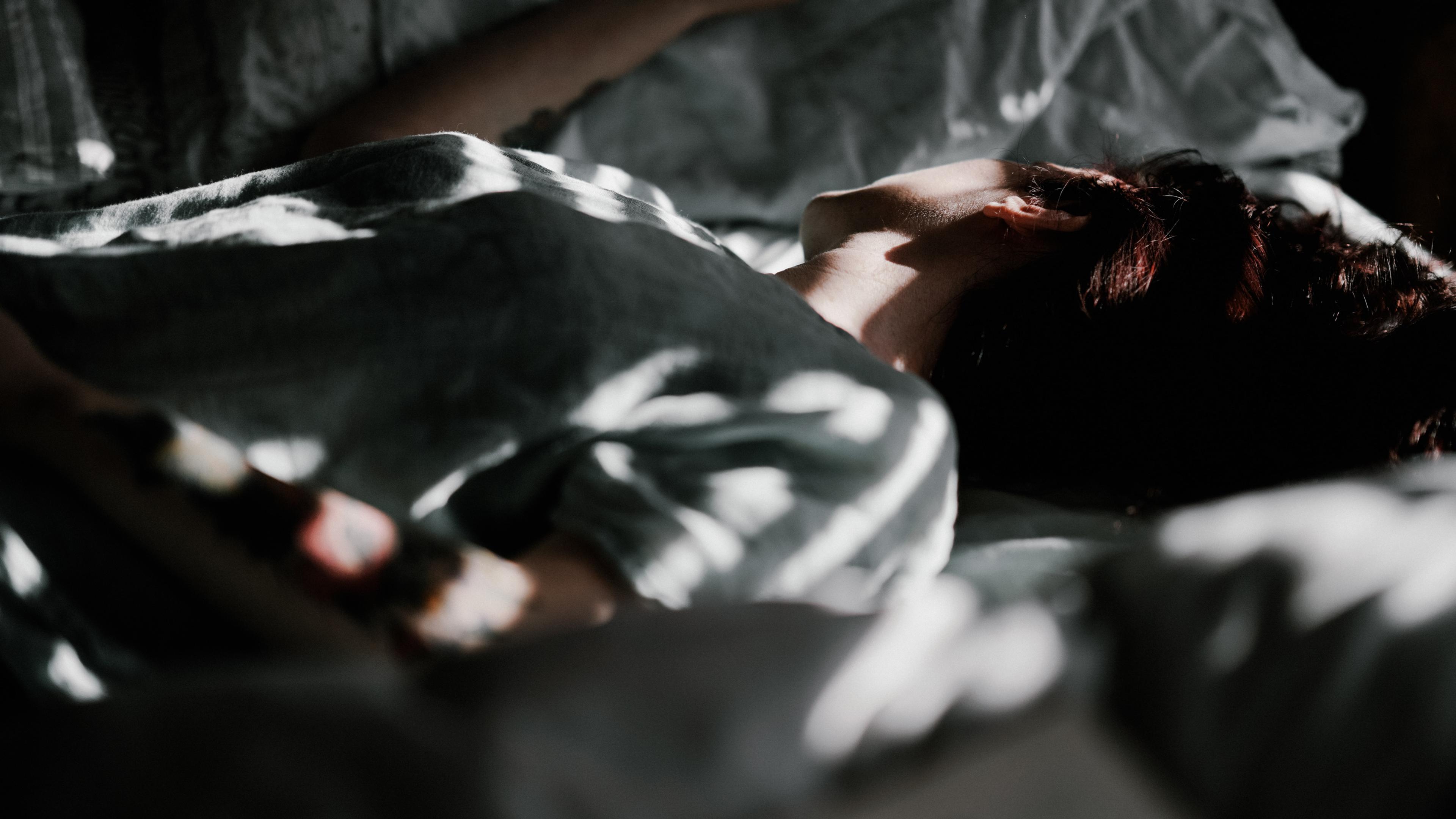 Photo of a person lying in bed under soft light and shadows, with focus on their neck and shoulder.