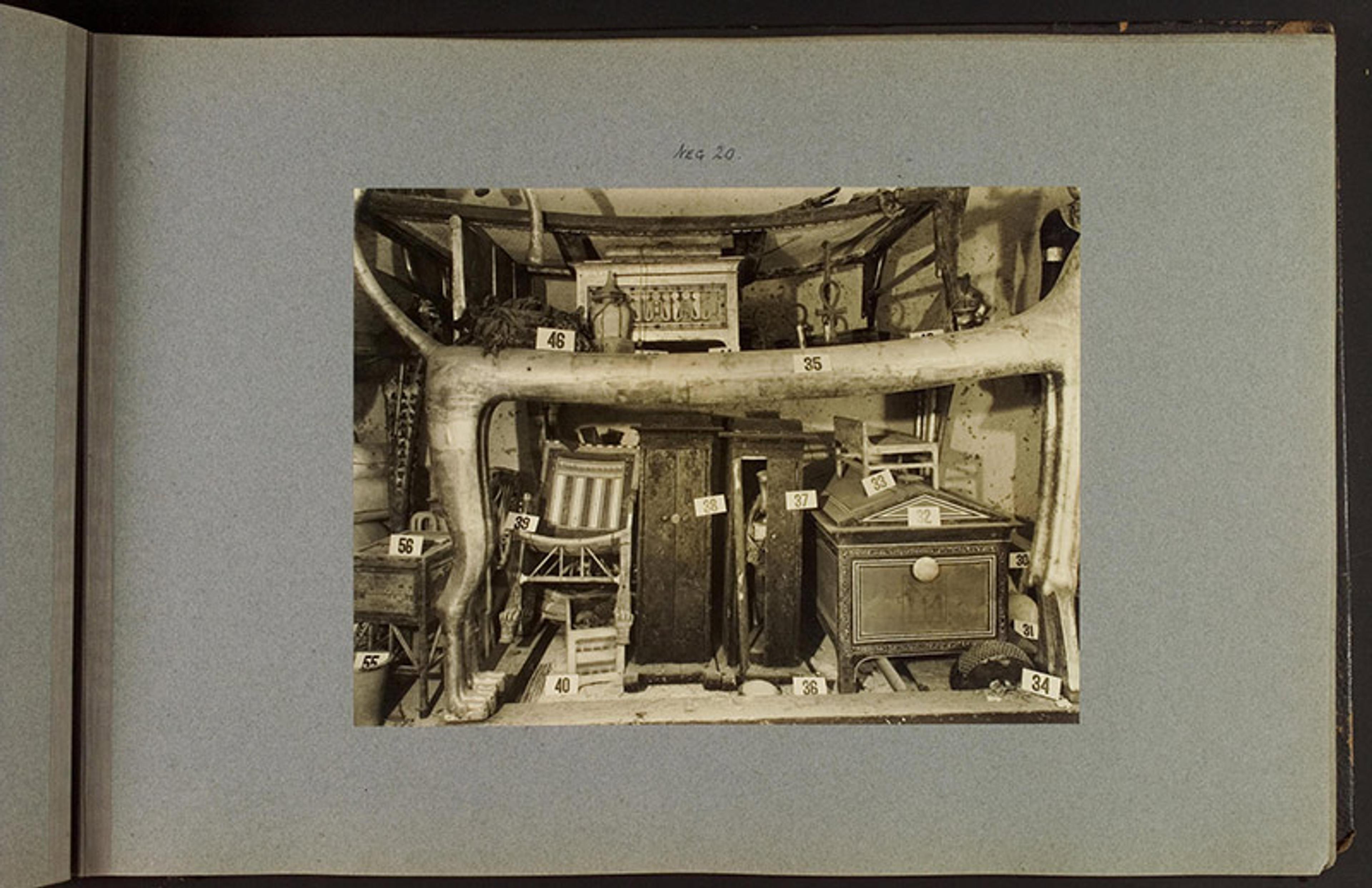 A sepia-toned photo of an artefact display including various furniture pieces, each labelled with numbers, placed on a light blue background.