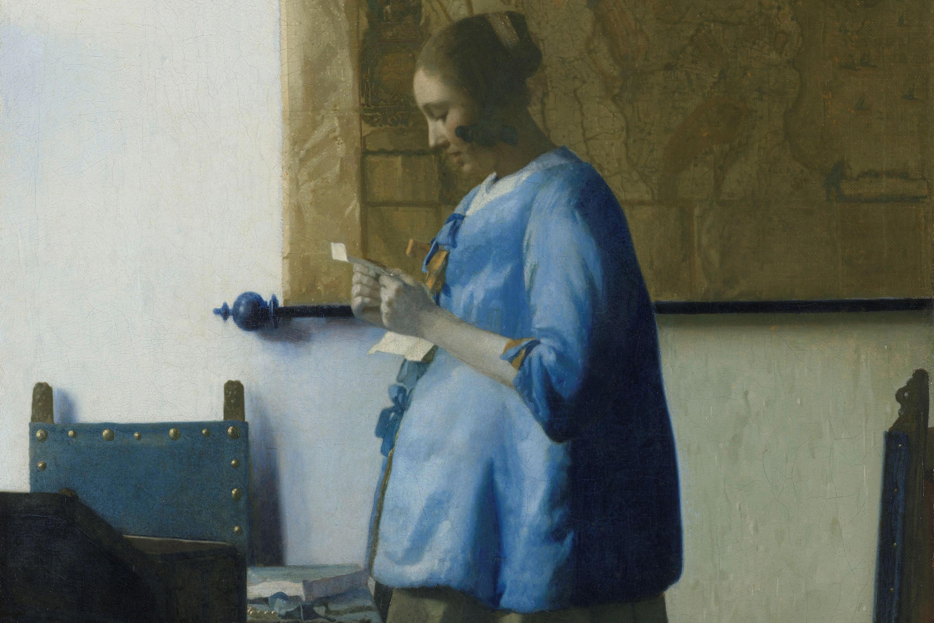 Painting of a woman in a blue dress reading a letter by a table with a large map on the wall behind her.