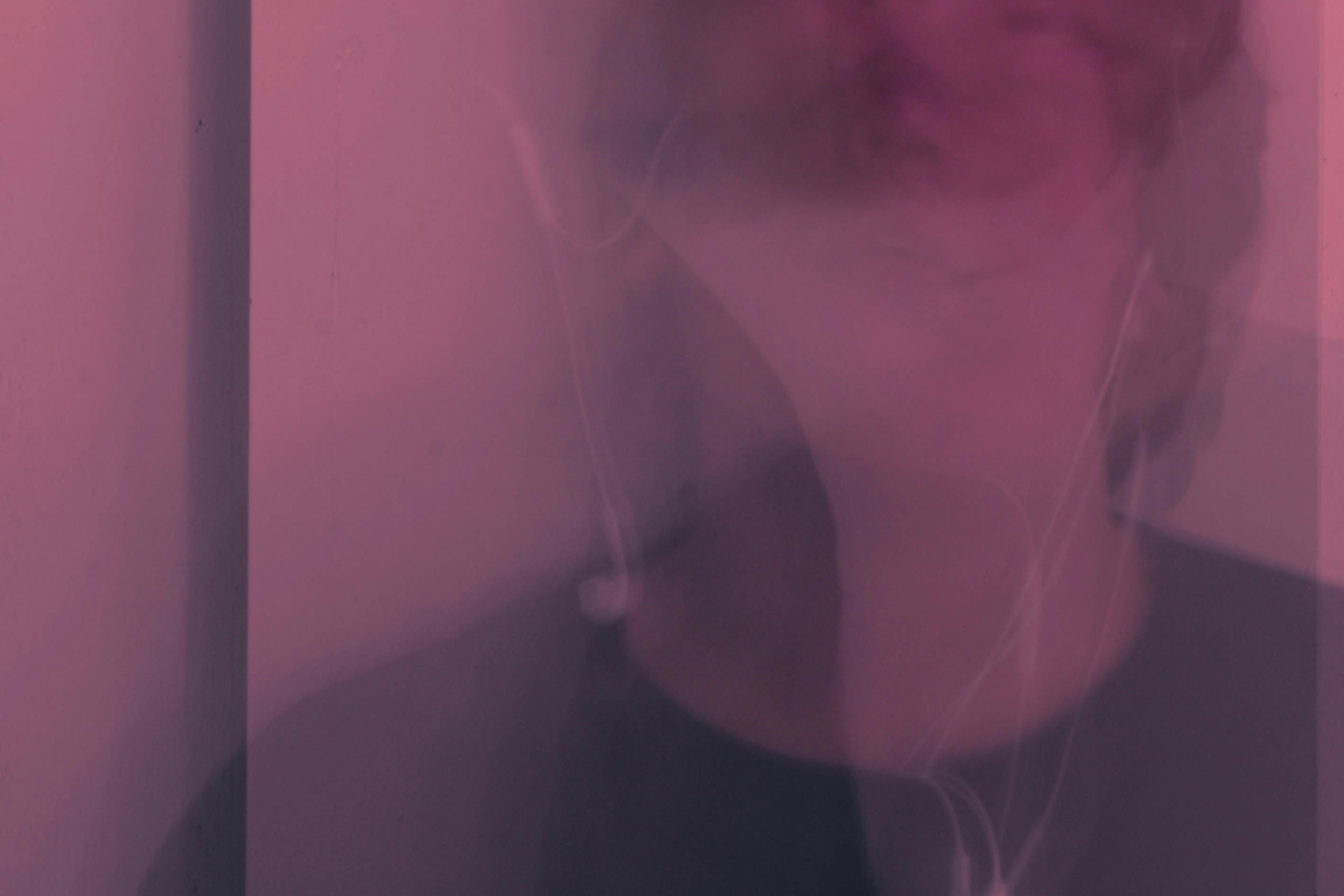 Abstract photo with a pink hue showing a blurred face and earphones.