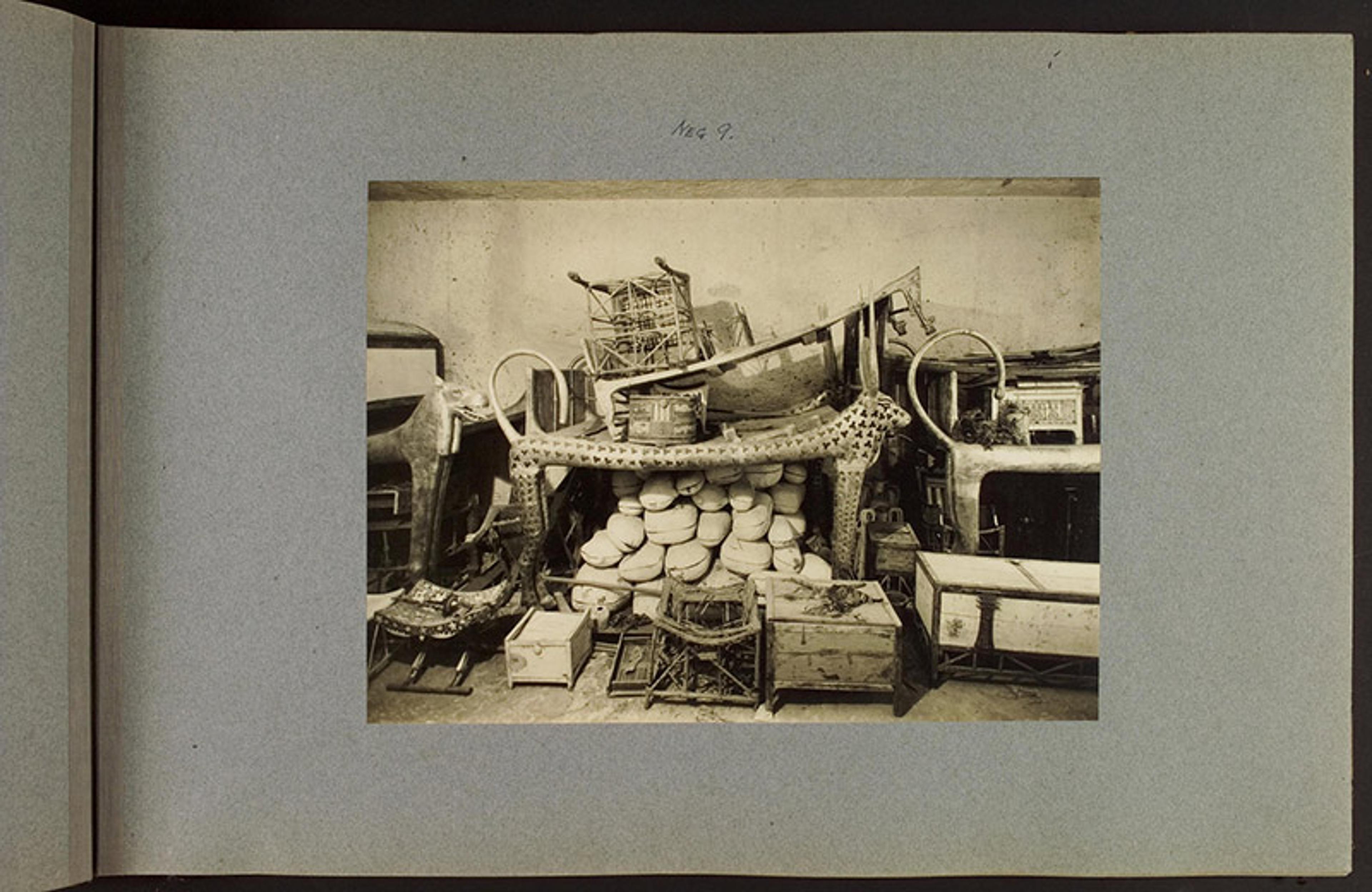 Black and white photo of ancient Egyptian artefacts in a cluttered storage room including statues, chests and various objects.