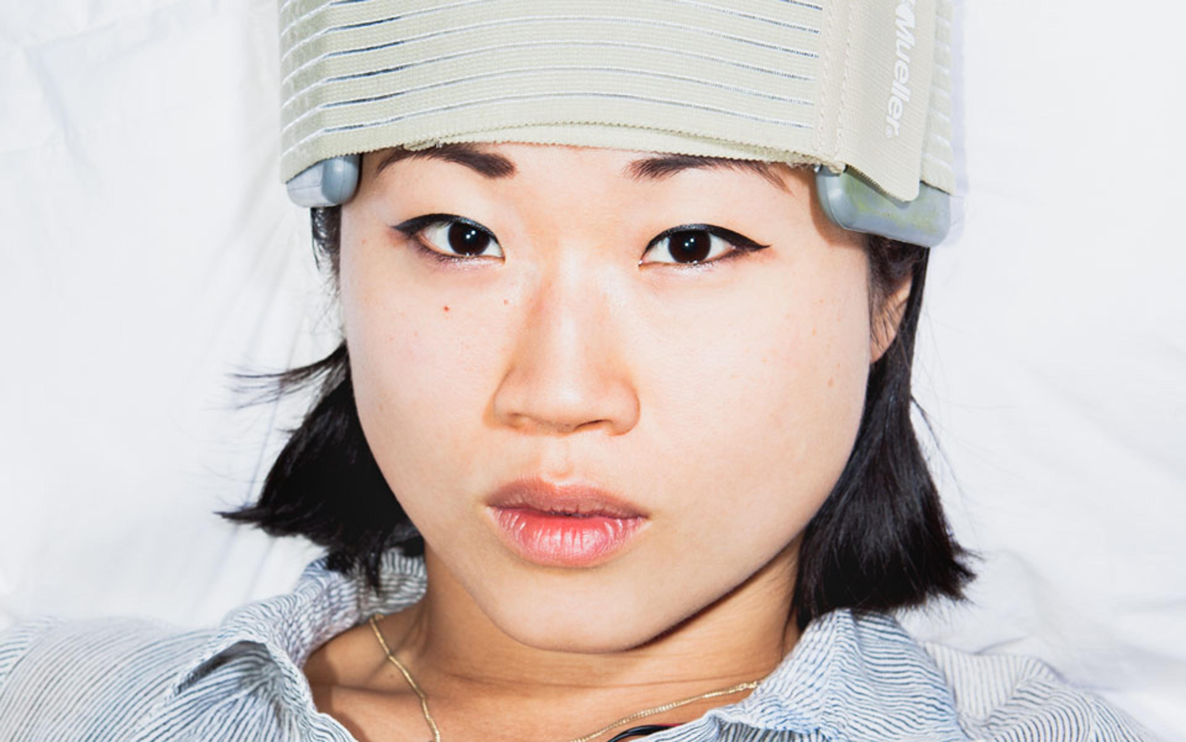 A woman lying down wearing a grey striped headband and a striped shirt, looking directly at the camera.