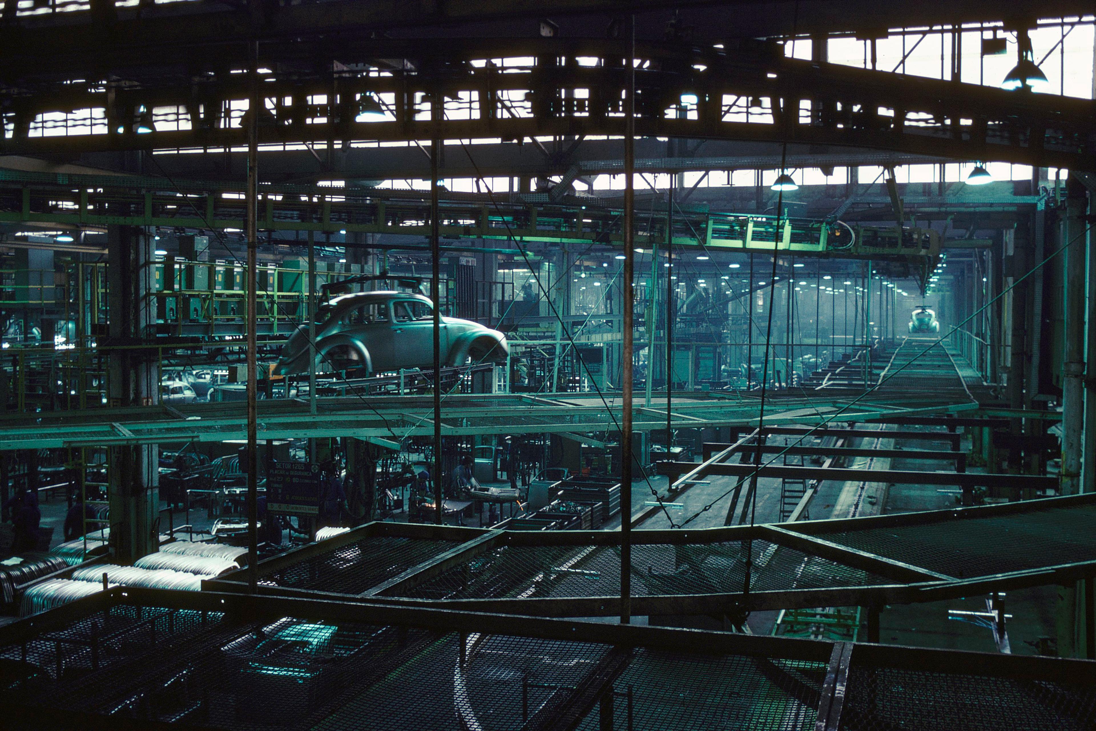 An automotive factory interior with a car body on an overhead conveyor, surrounded by industrial machinery.