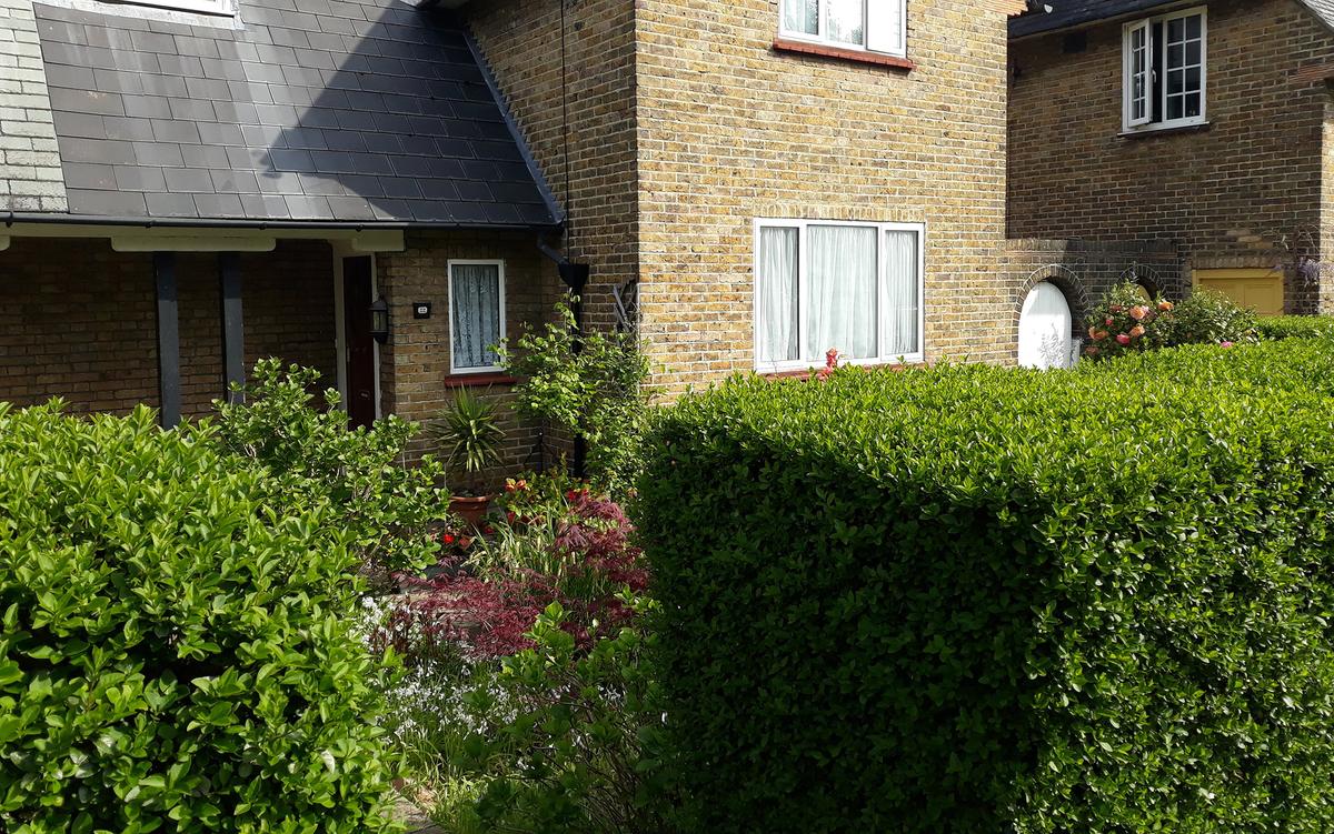 A brick house with a tiled roof, surrounded by a well-maintained garden with bushes and colourful flowers.