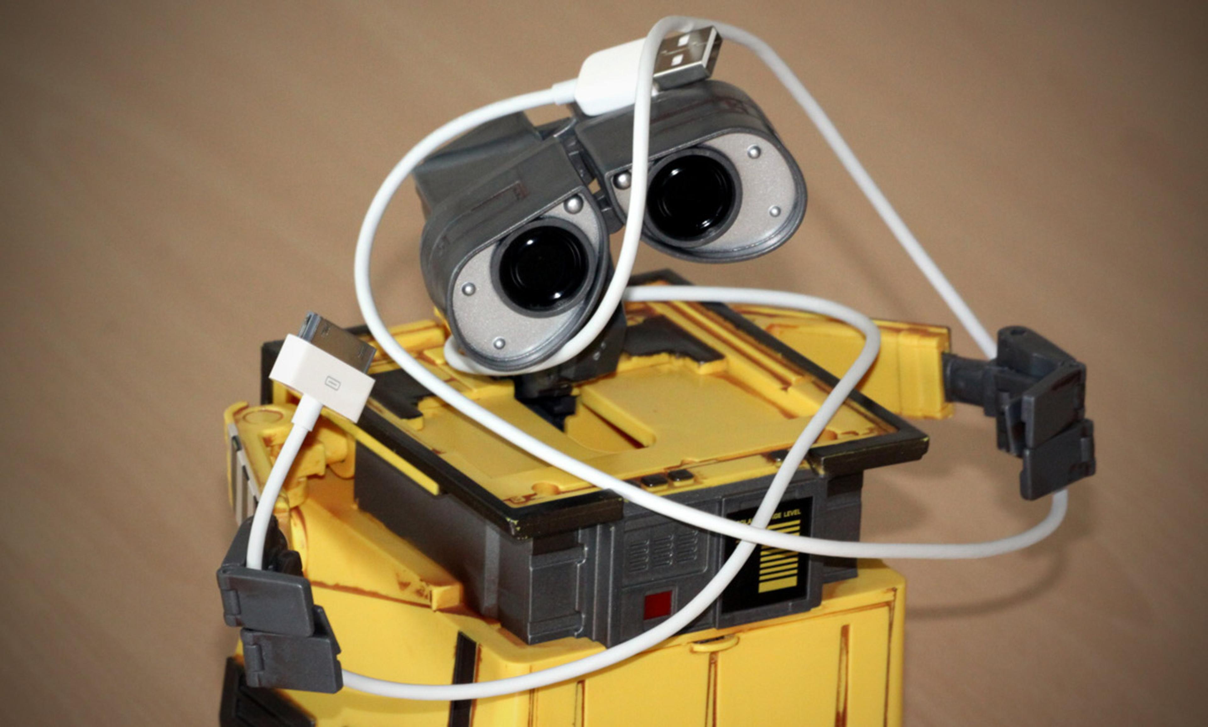 A toy robot with binocular-like eyes tangled in a white USB cable, set against a blurred brown background.