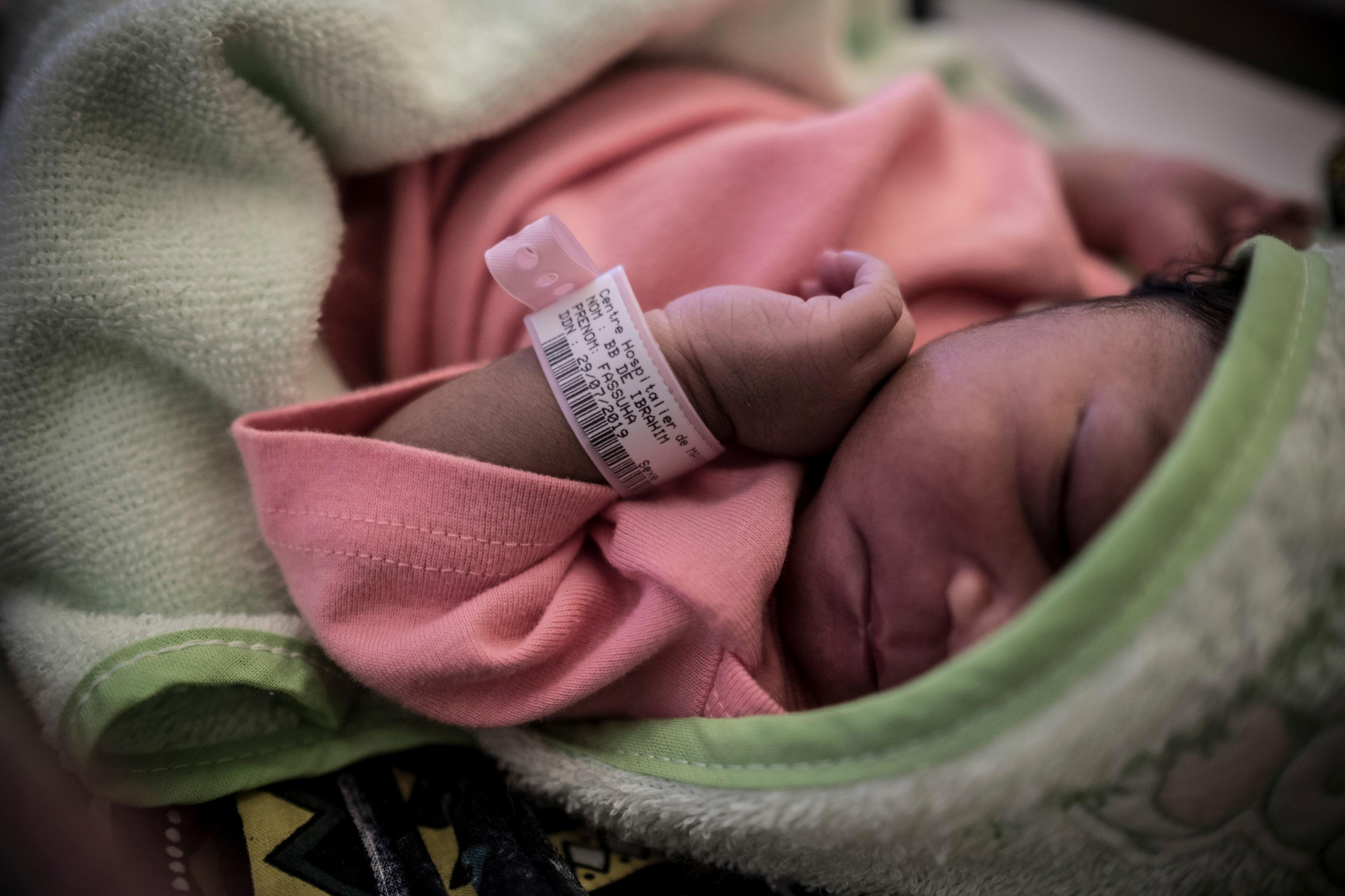 Photo of a sleeping newborn in pink wrapped in a green blanket wearing a medical ID bracelet on their wrist.