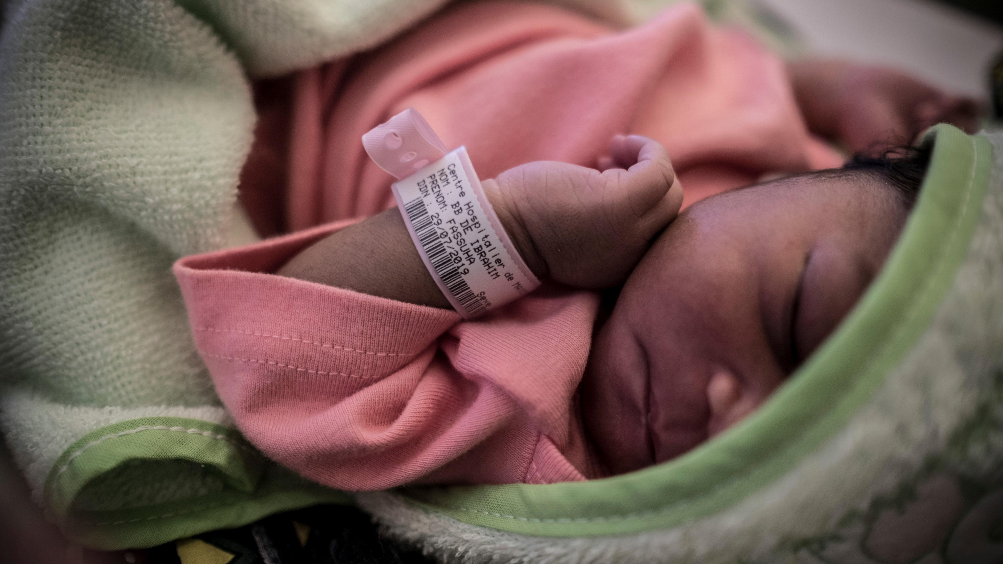 Photo of a sleeping newborn in pink wrapped in a green blanket wearing a medical ID bracelet on their wrist.