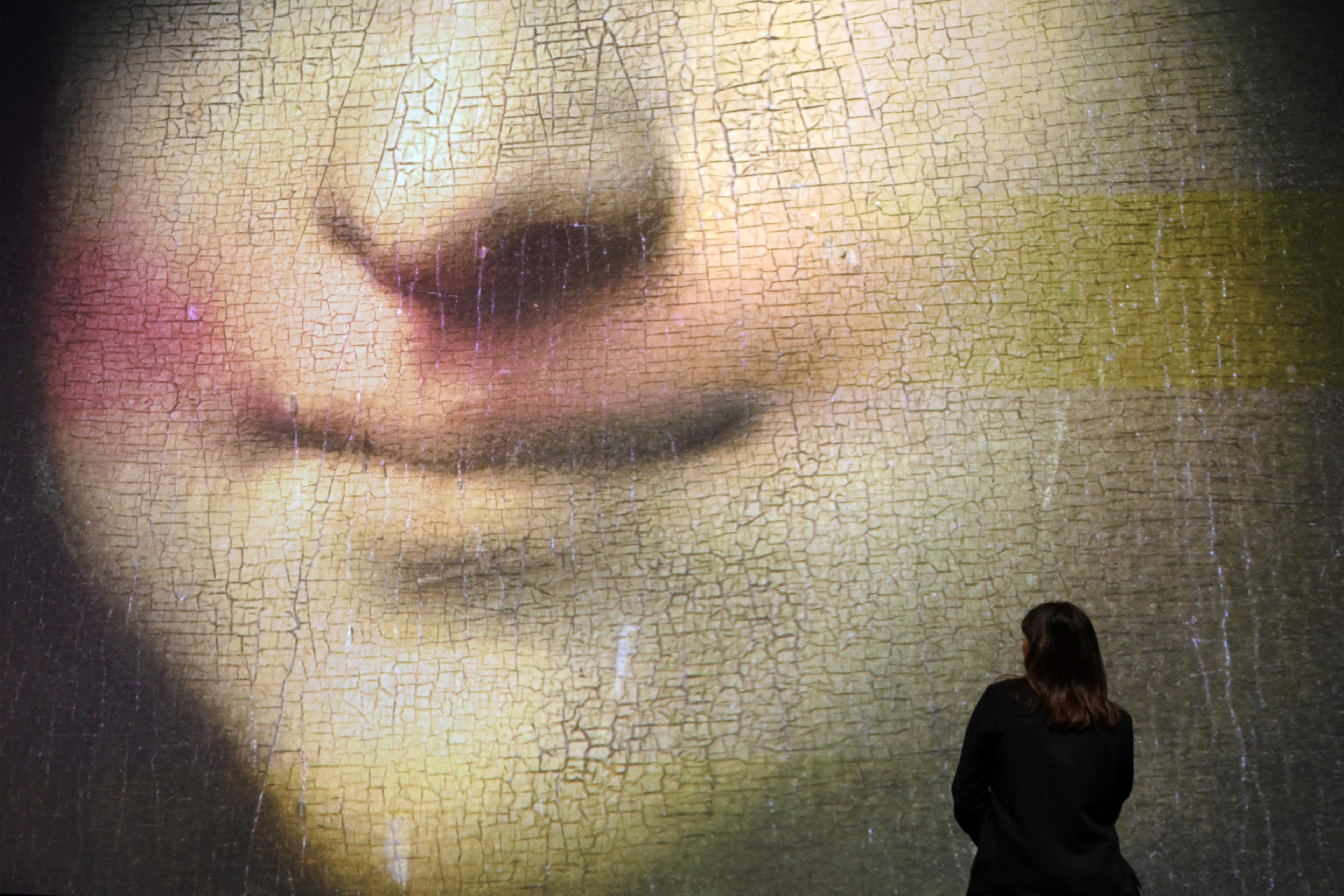 Large projection of a painting’s cracked surface with a person standing in front, focusing on a close-up of a smiling mouth.