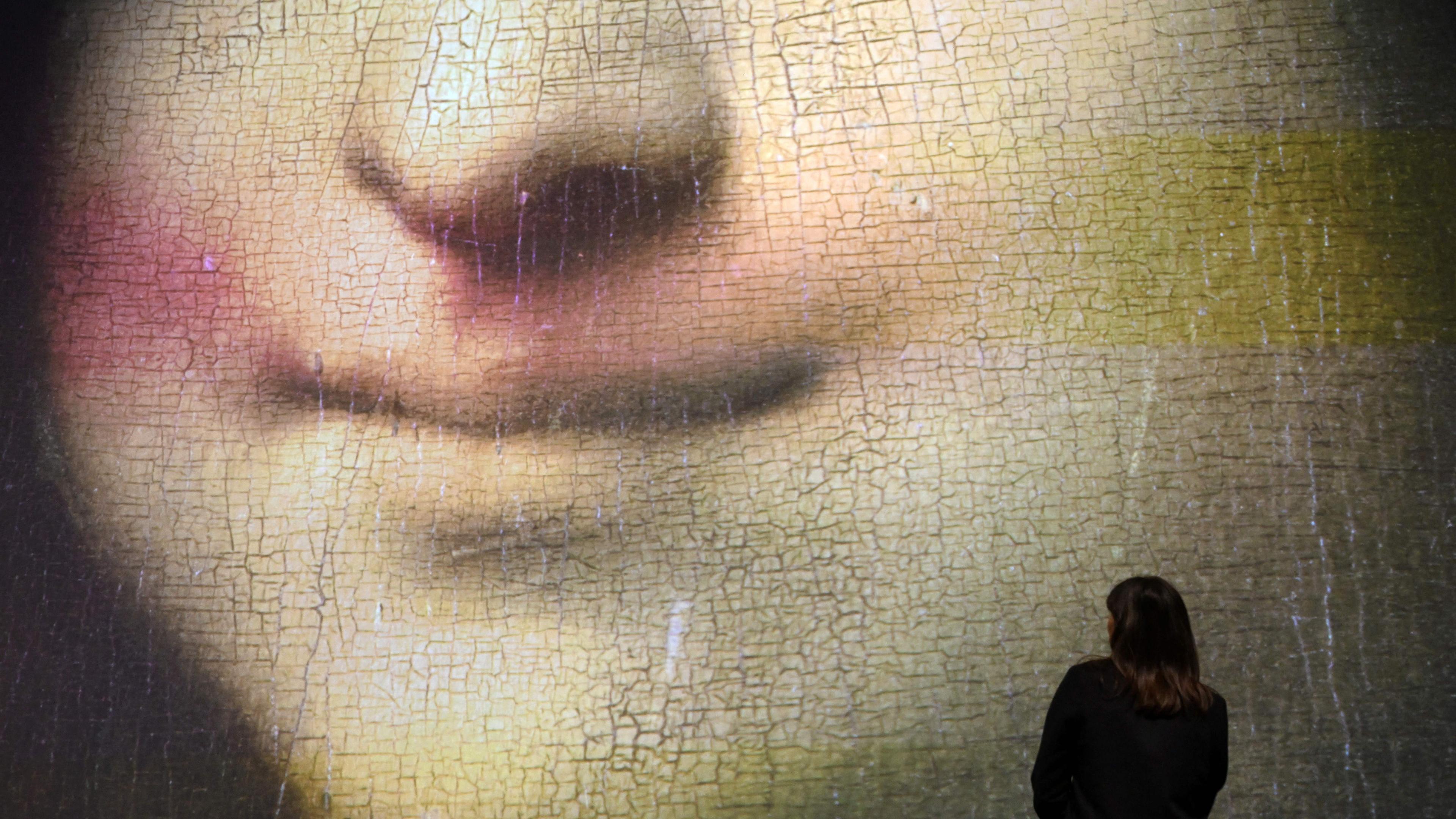 Large projection of a painting’s cracked surface with a person standing in front, focusing on a close-up of a smiling mouth.