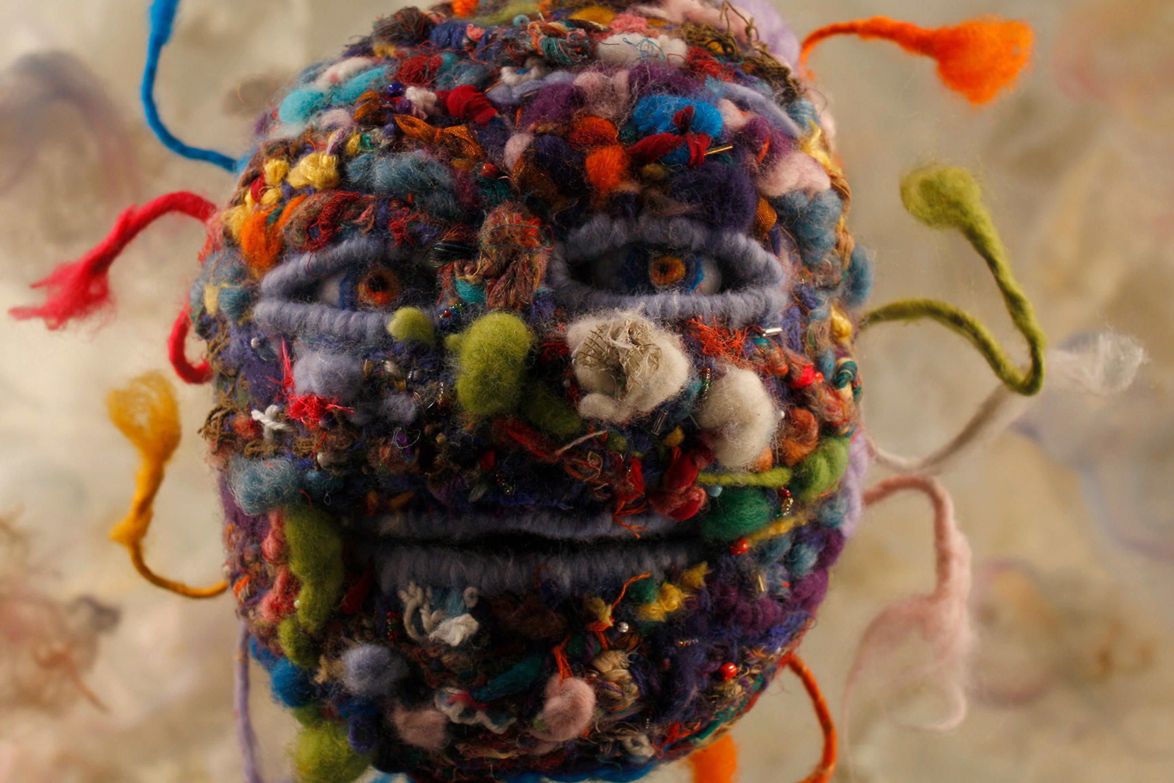 Close-up of a colourful, abstract wool sculpture resembling a face with various textures and fibres extending outward.