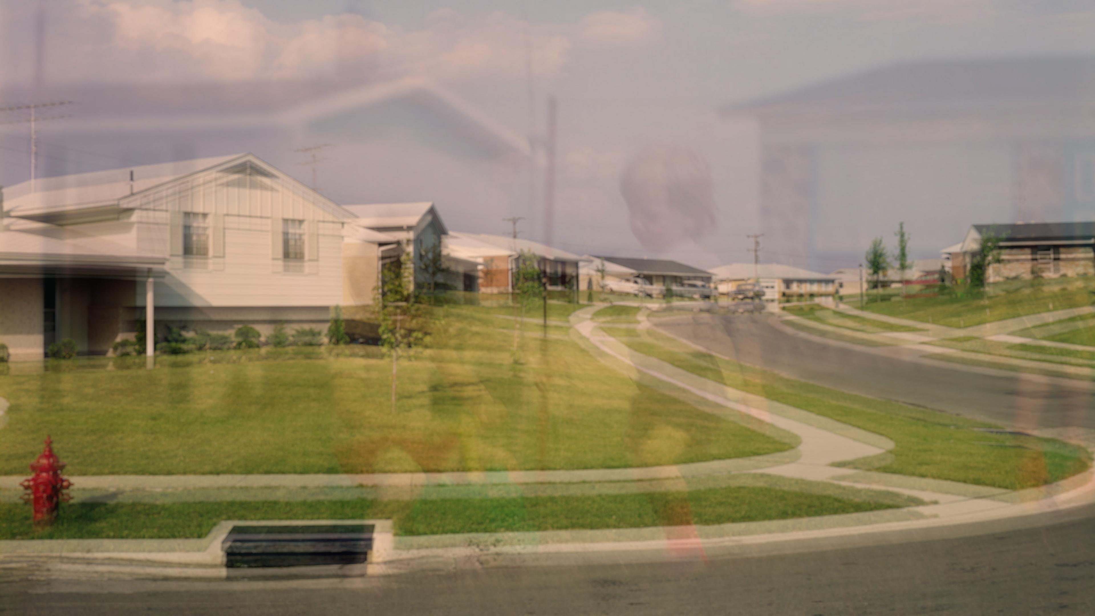 Photo of a suburban street with overlapping images, showing houses, lawns and a faint figure in the foreground.