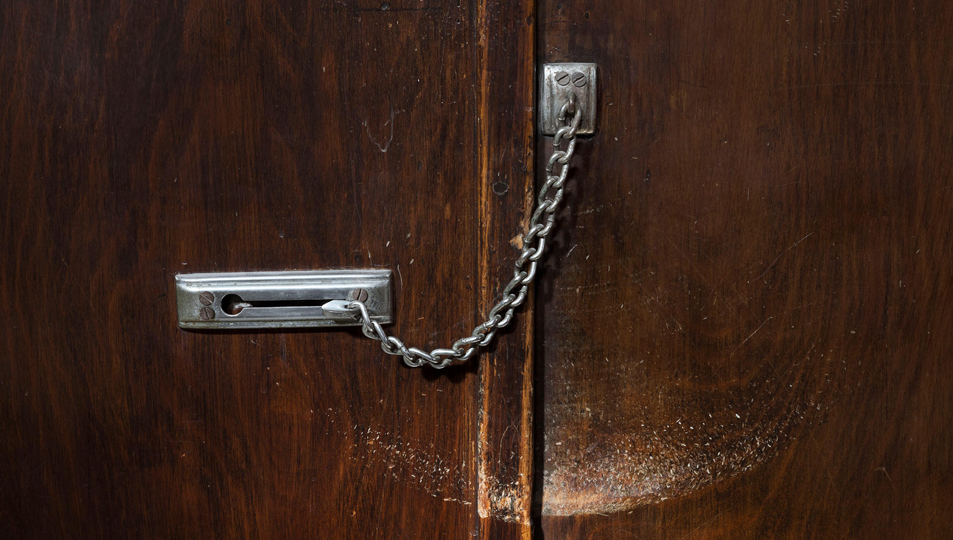 Close-up of a closed metal door-chain on a wooden door