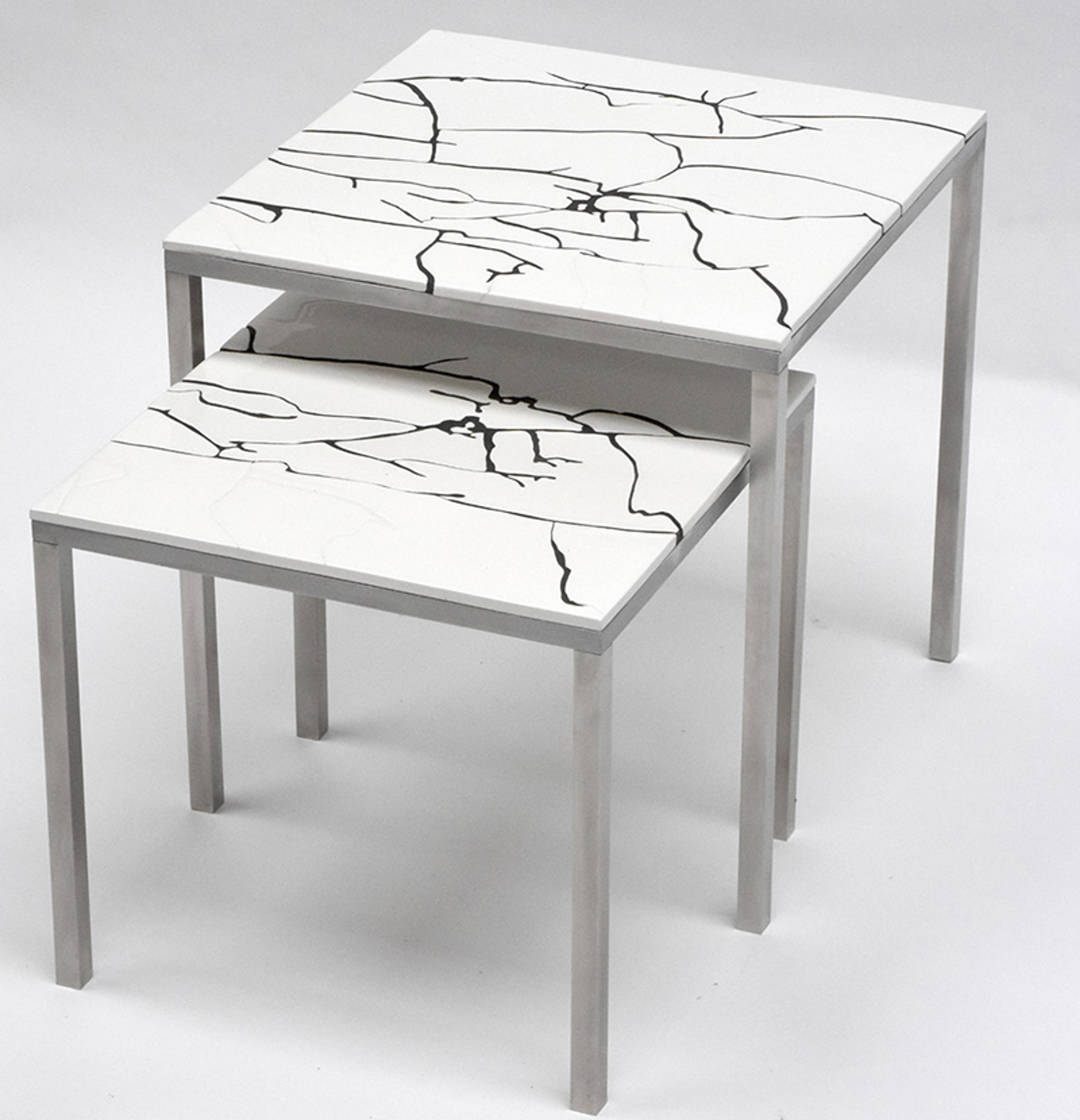 Two nesting tables with white tops featuring black crack-like patterns, and metal legs positioned against a white background.