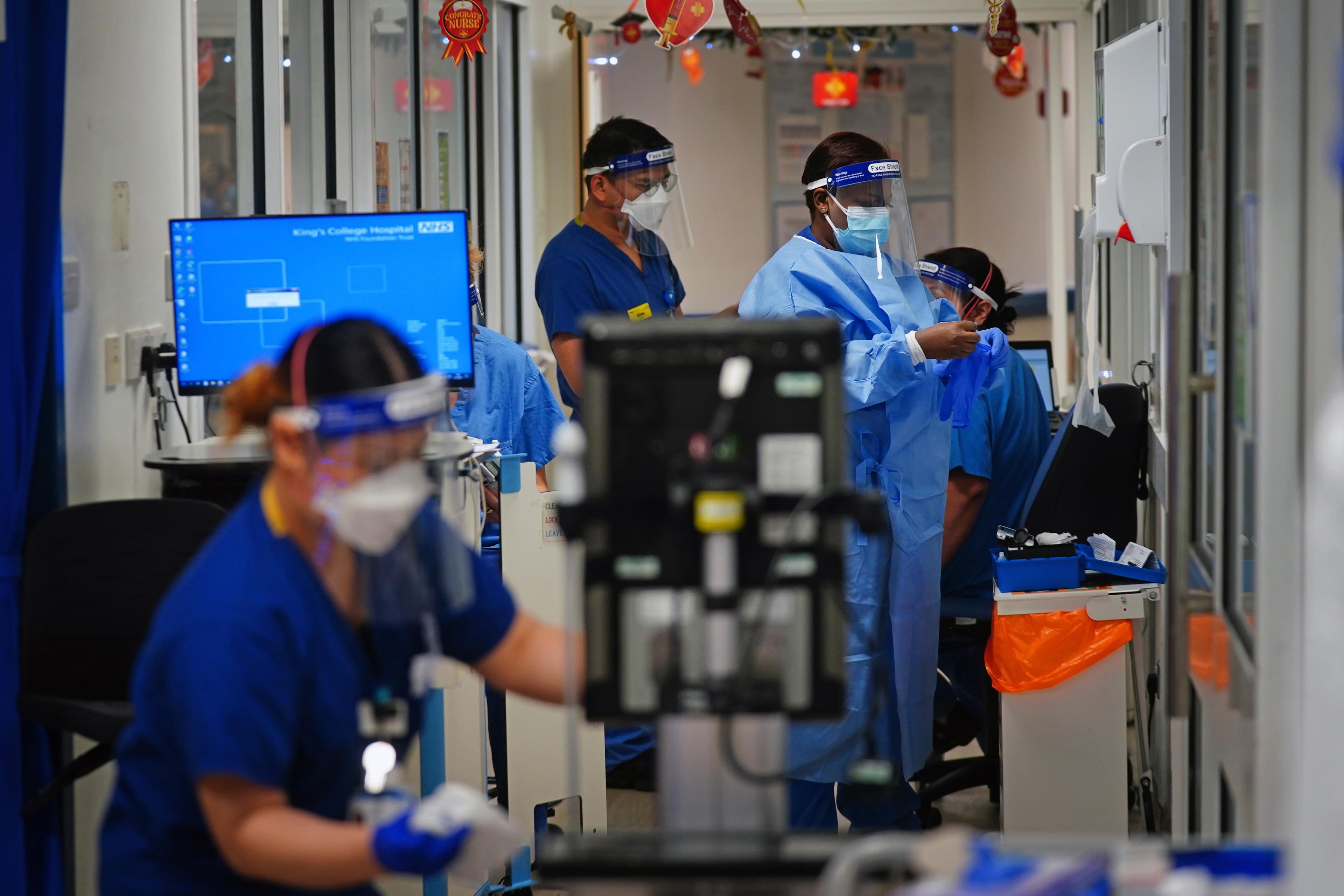 Photo of medical staff in PPE working in a hospital ward with computers and monitors visible in the background.
