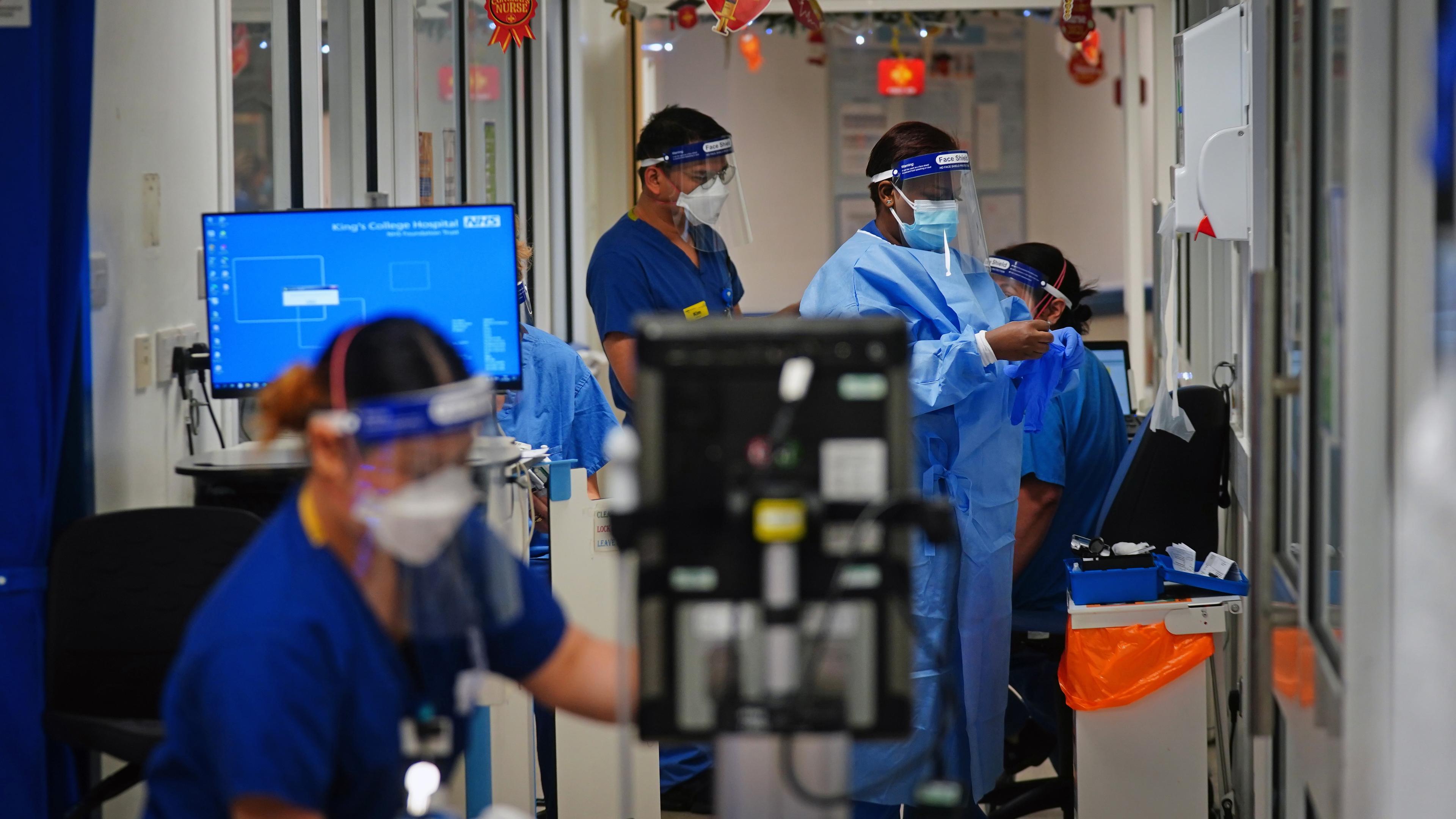 Photo of medical staff in PPE working in a hospital ward with computers and monitors visible in the background.