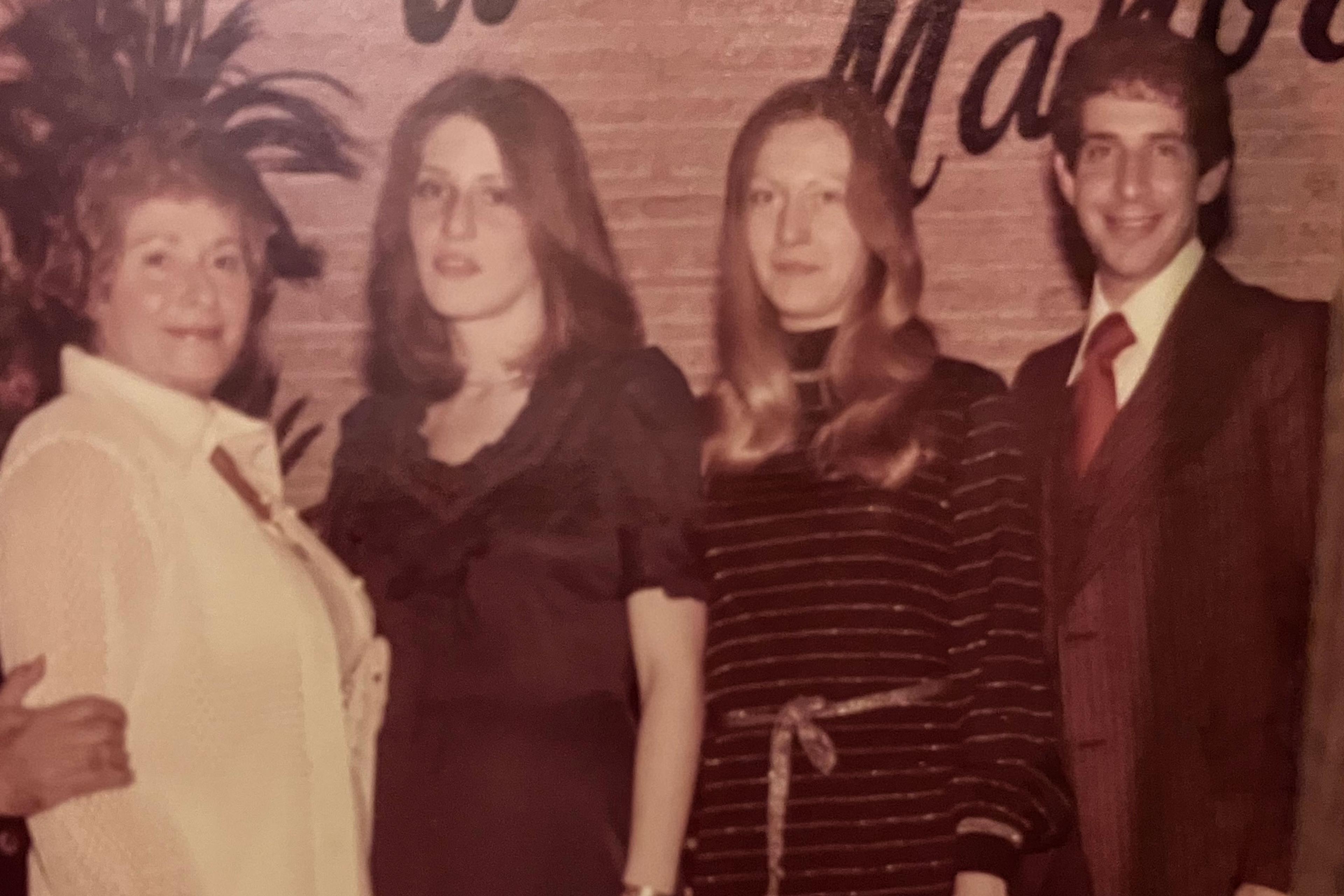 Vintage photo of four people posing indoors with a plant and brick wall background.