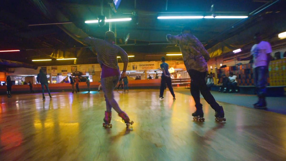 Photo of people roller skating on a wooden rink under neon lights in an indoor facility.