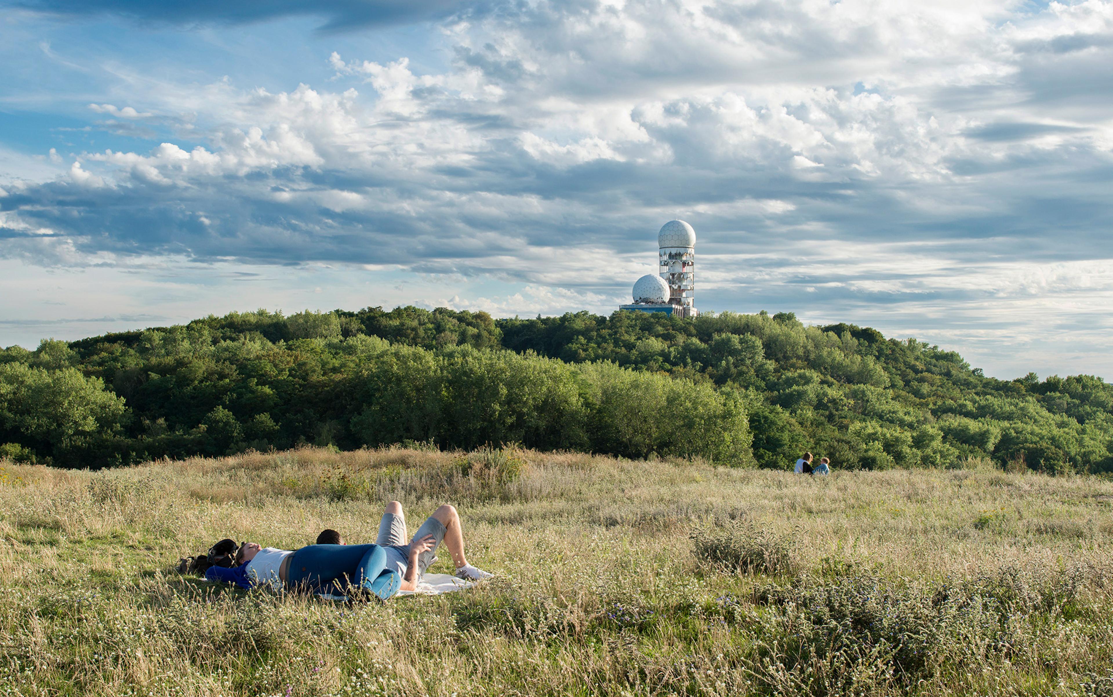 A couple lying on grass on a hill nearby an American listening station in Berlin