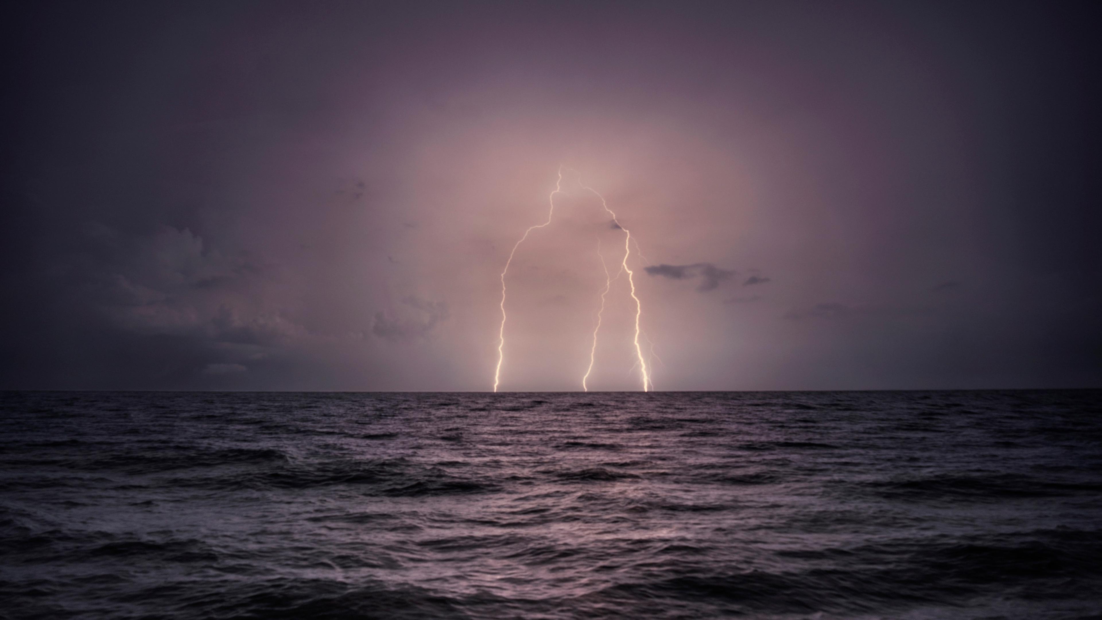 Photo of a dark ocean at night with two lightning strikes illuminating the cloudy sky.