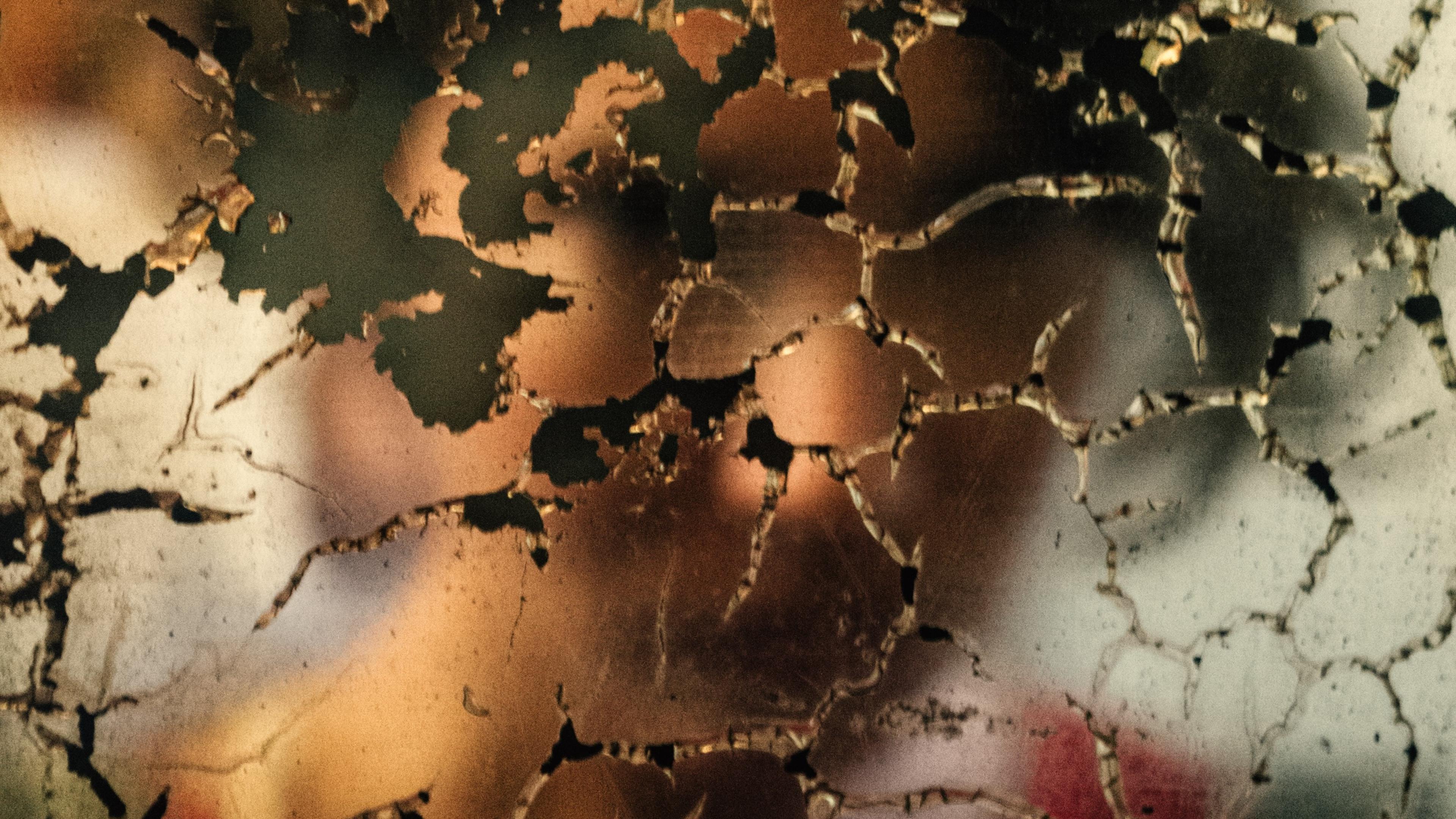 Photo of a blurred background visible through cracked peeling paint on a surface in earthy tones.