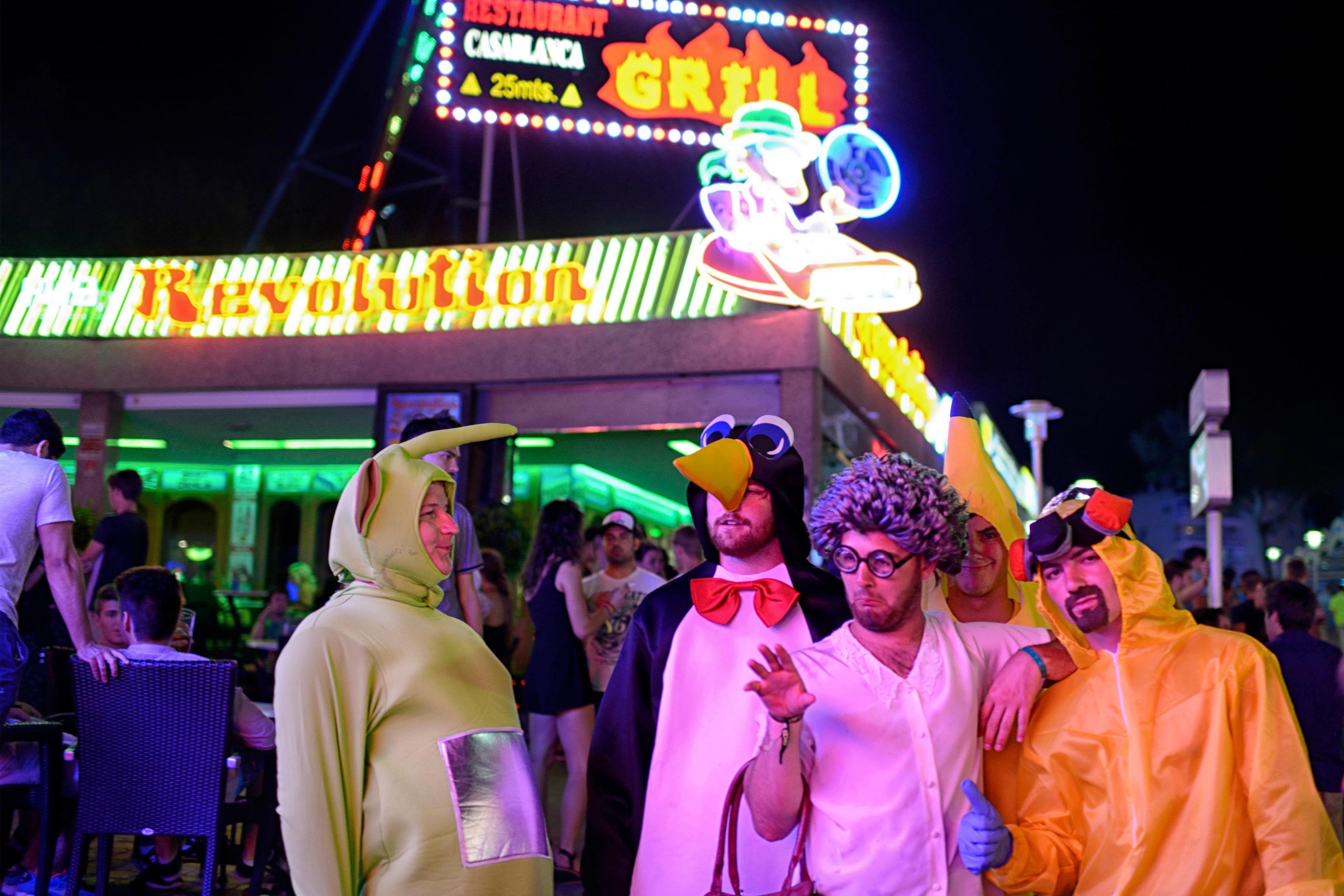 Photo of people in colourful costumes at night outside a neon-lit restaurant.
