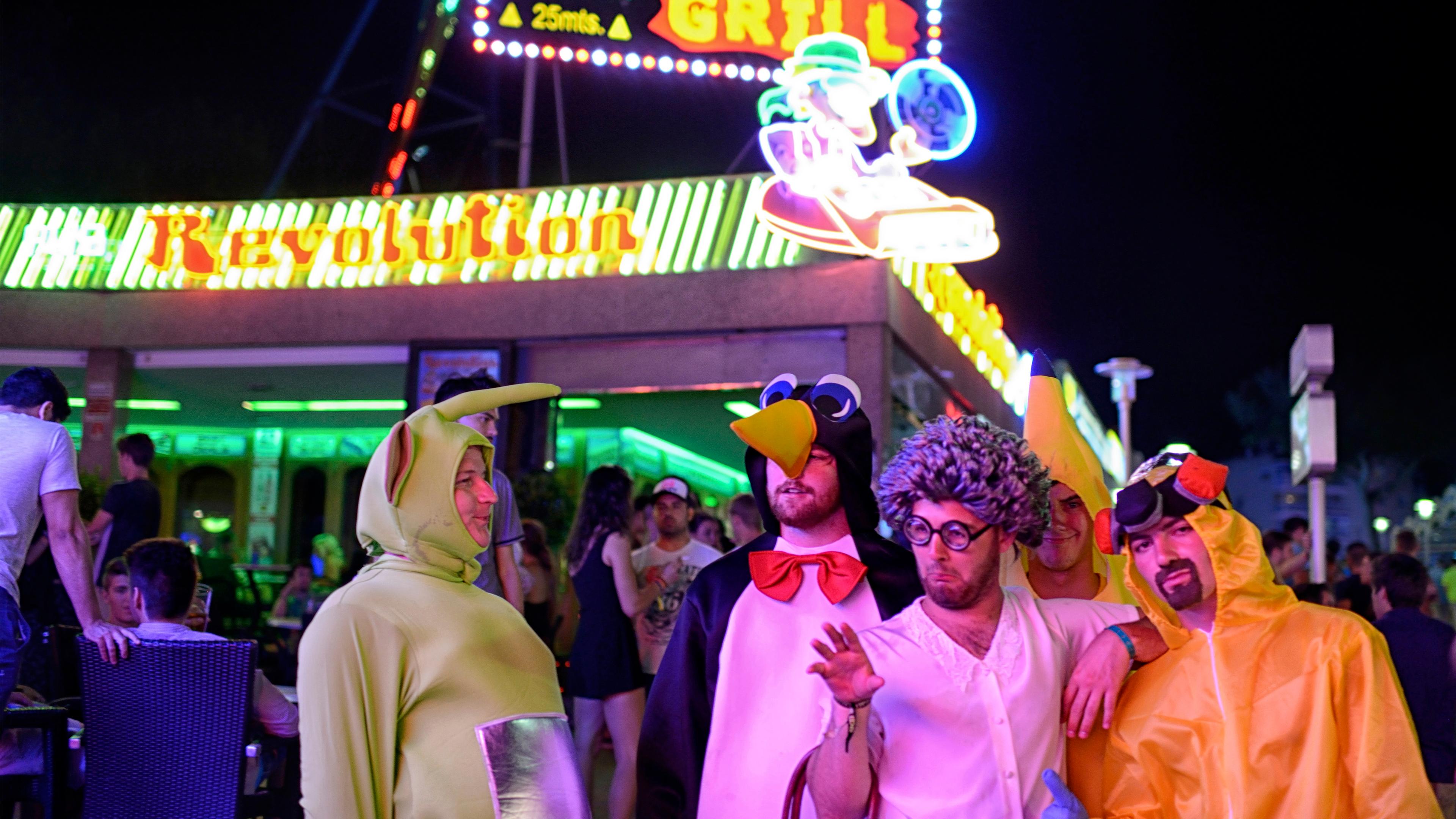 Photo of people in colourful costumes at night outside a neon-lit restaurant.