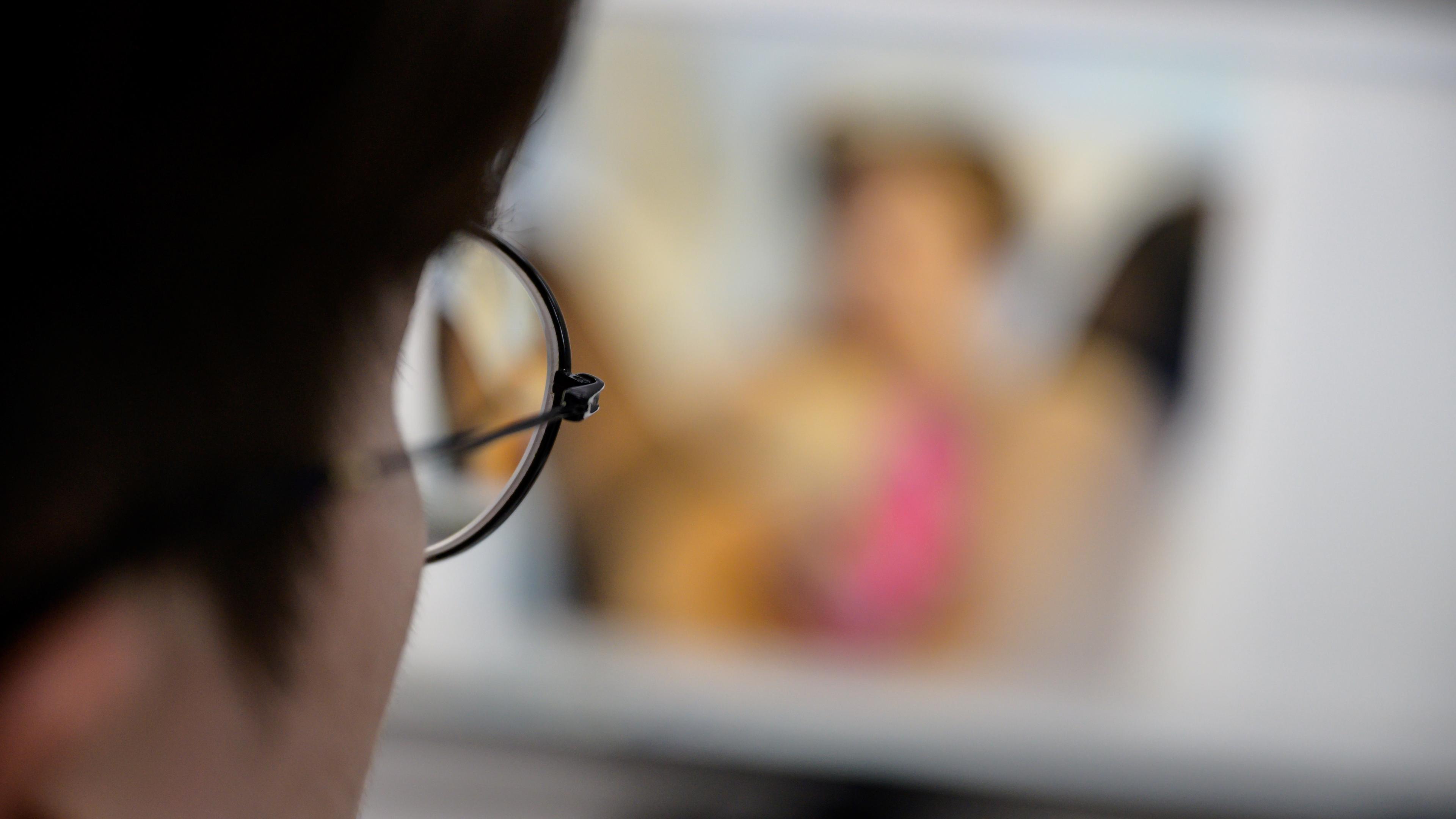 Photo of a person wearing glasses viewing a blurred screen focus on glasses frame.