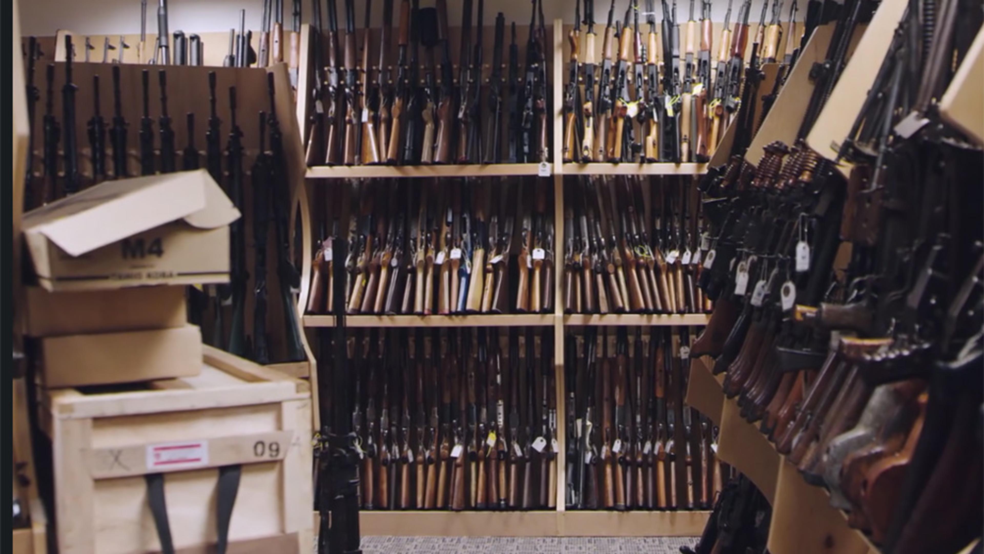A storeroom filled with rifles on shelves and boxes labelled ‘M4’. The room is well-lit and the rifles appear organised.
