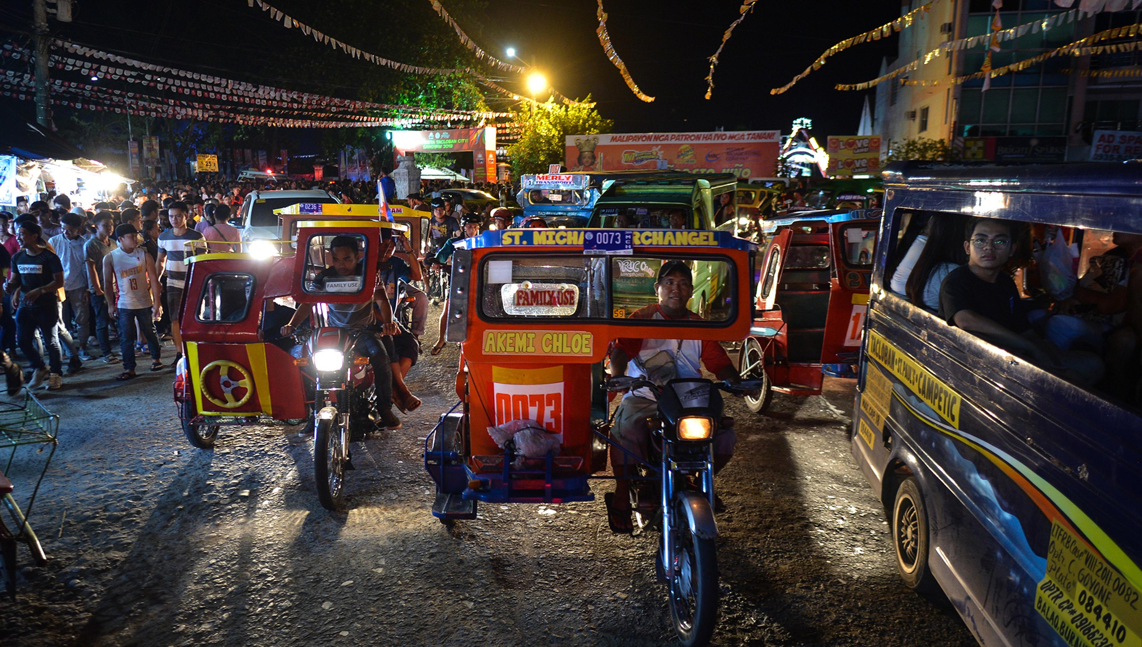 Photo of a busy night street market with people and colourful tricycles in the Philippines, lit by street lights and signage.