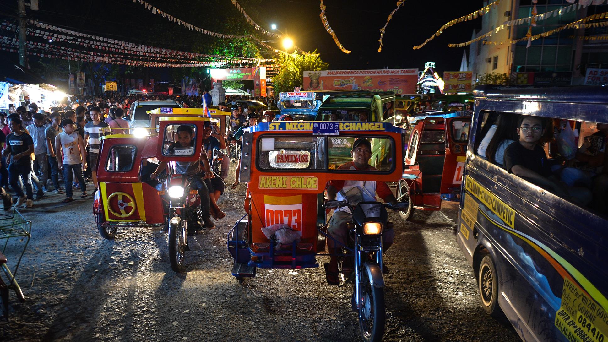 Photo of a busy night street market with people and colourful tricycles in the Philippines, lit by street lights and signage.