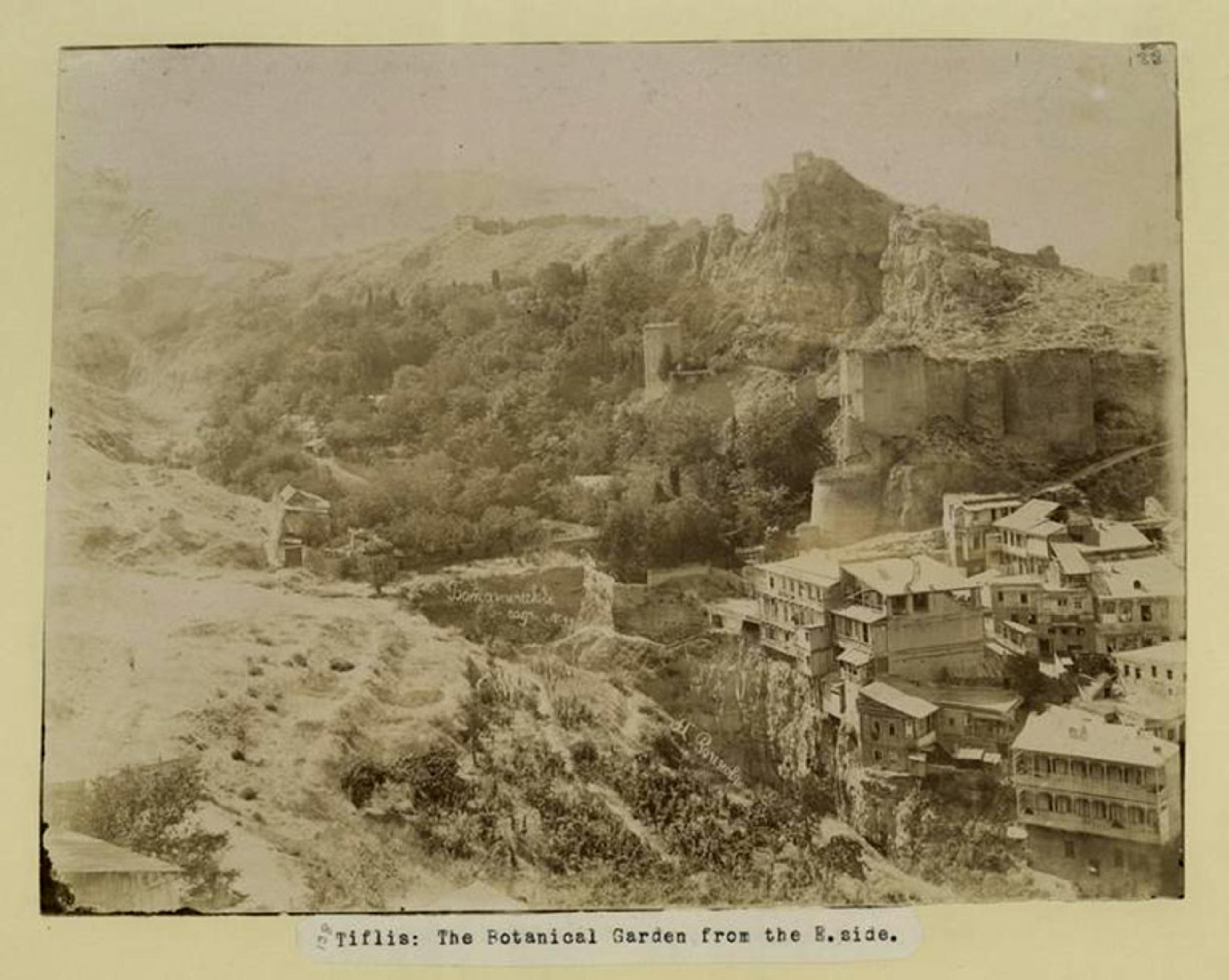 Old sepia-toned photograph of Tbilisi Botanical Garden from the east side, showing rugged terrain, greenery and historical buildings.